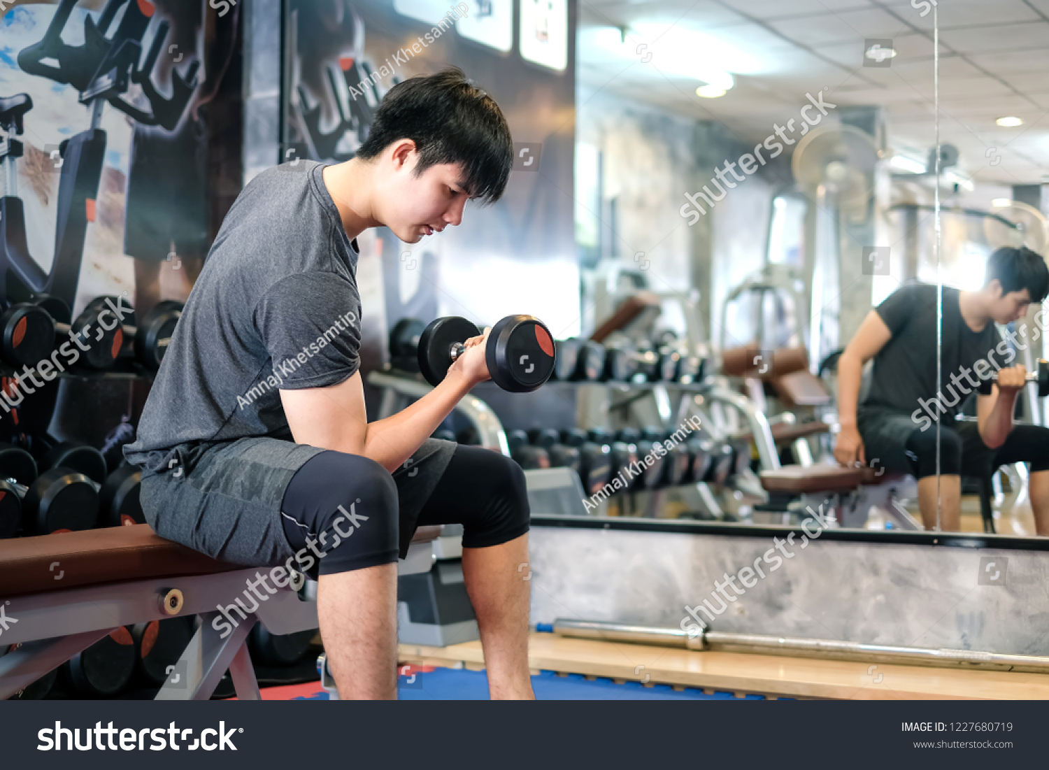 Asian man exercising using dumbbell in the gym. #1227680719