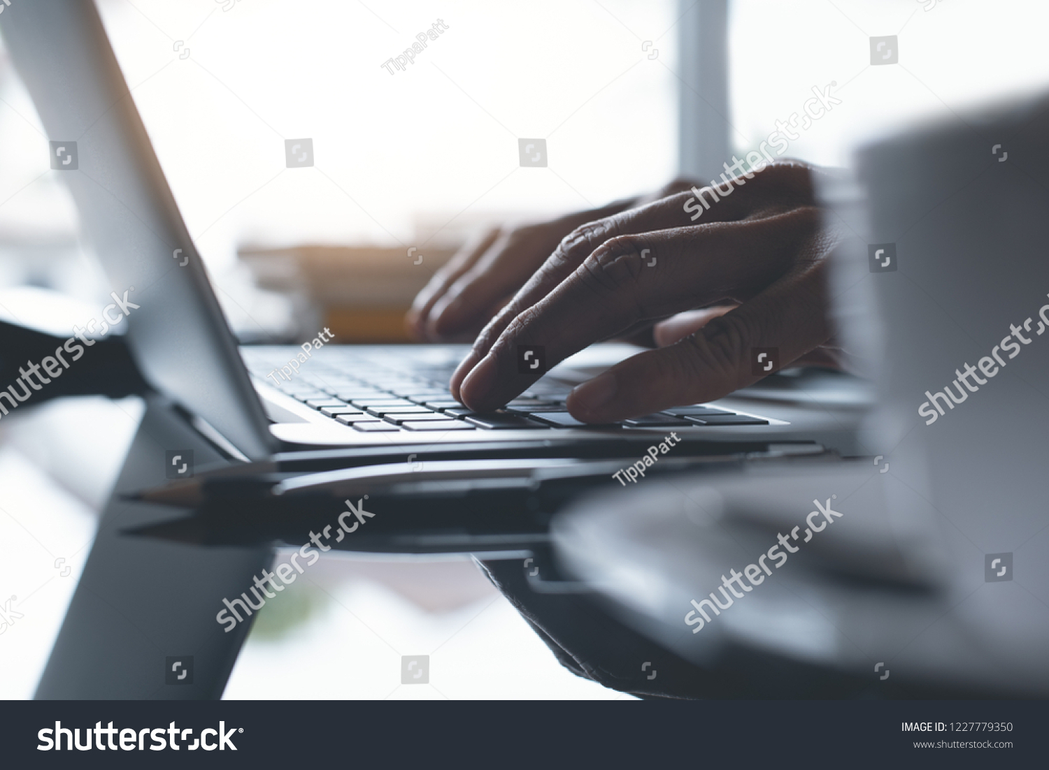 Freelance man working on laptop computer with cup of coffee on desk at coffee shop or home office with morning sunlight, close up. Portable office, Online working concept. #1227779350