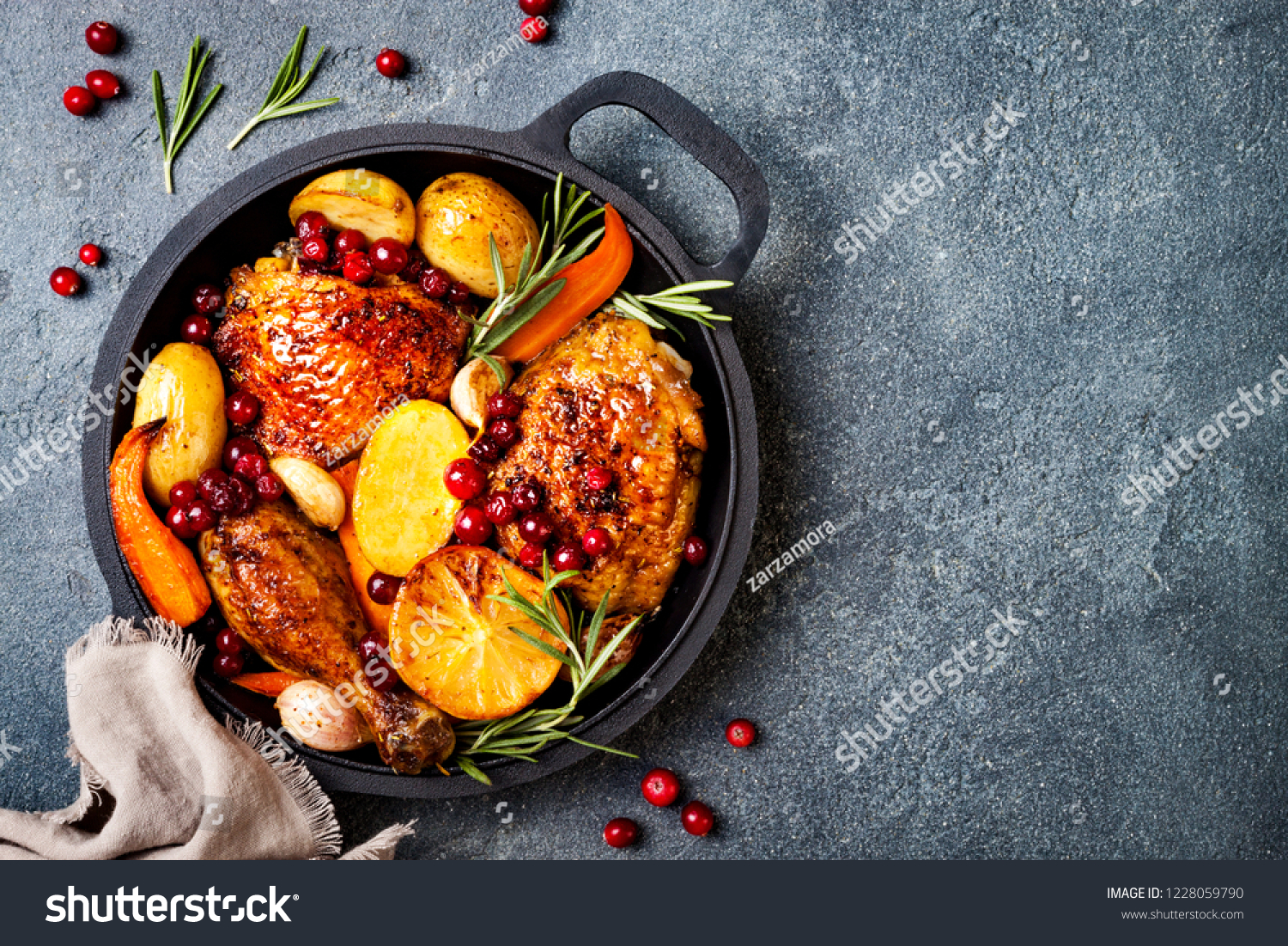 Roasted chicken legs with root vegetables, lemon, garlic, cranberry and rosemary on pan, on black slate stone background #1228059790