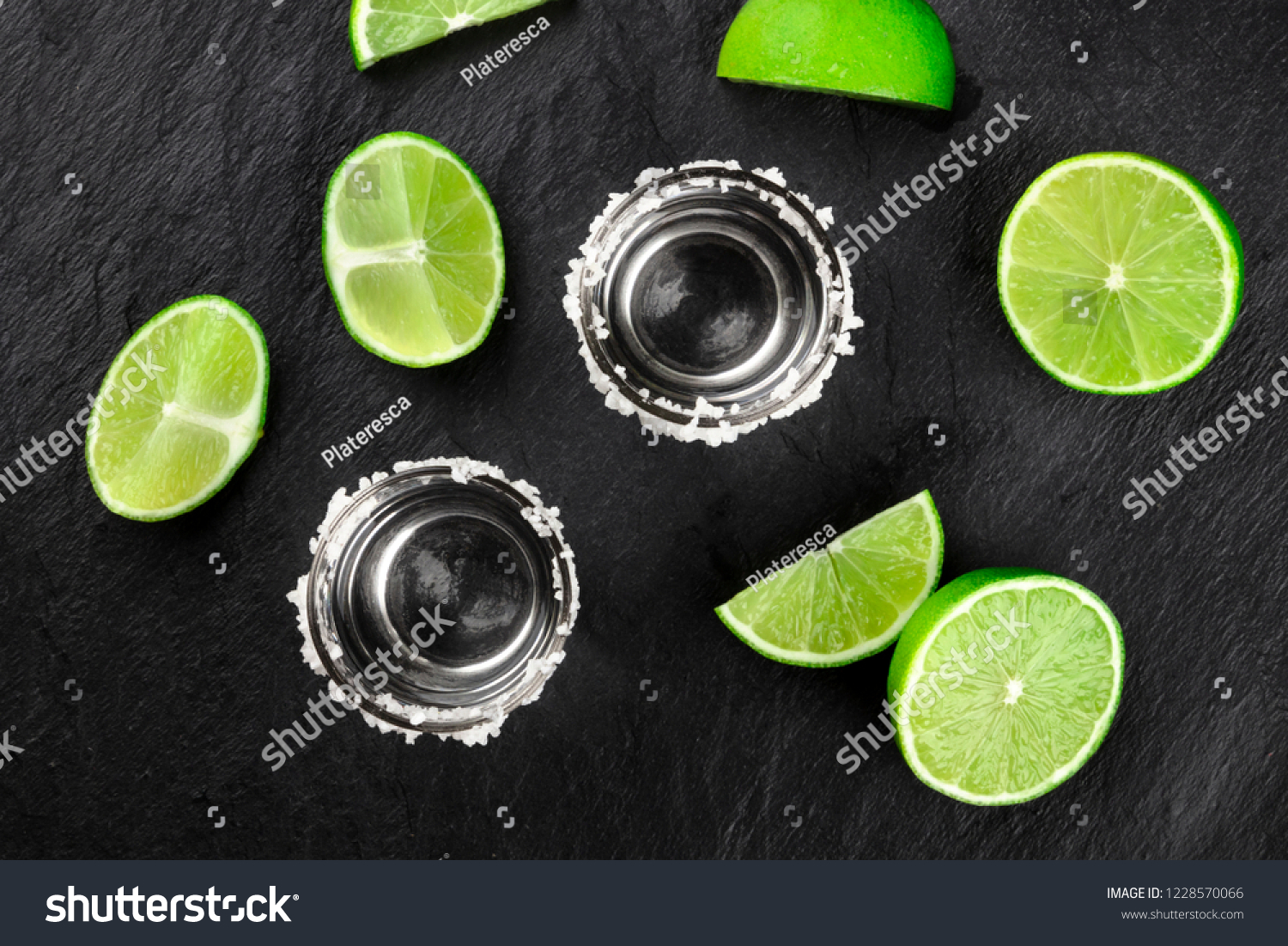 Two tequila shots with many lime slices, shot from the top on a dark background #1228570066