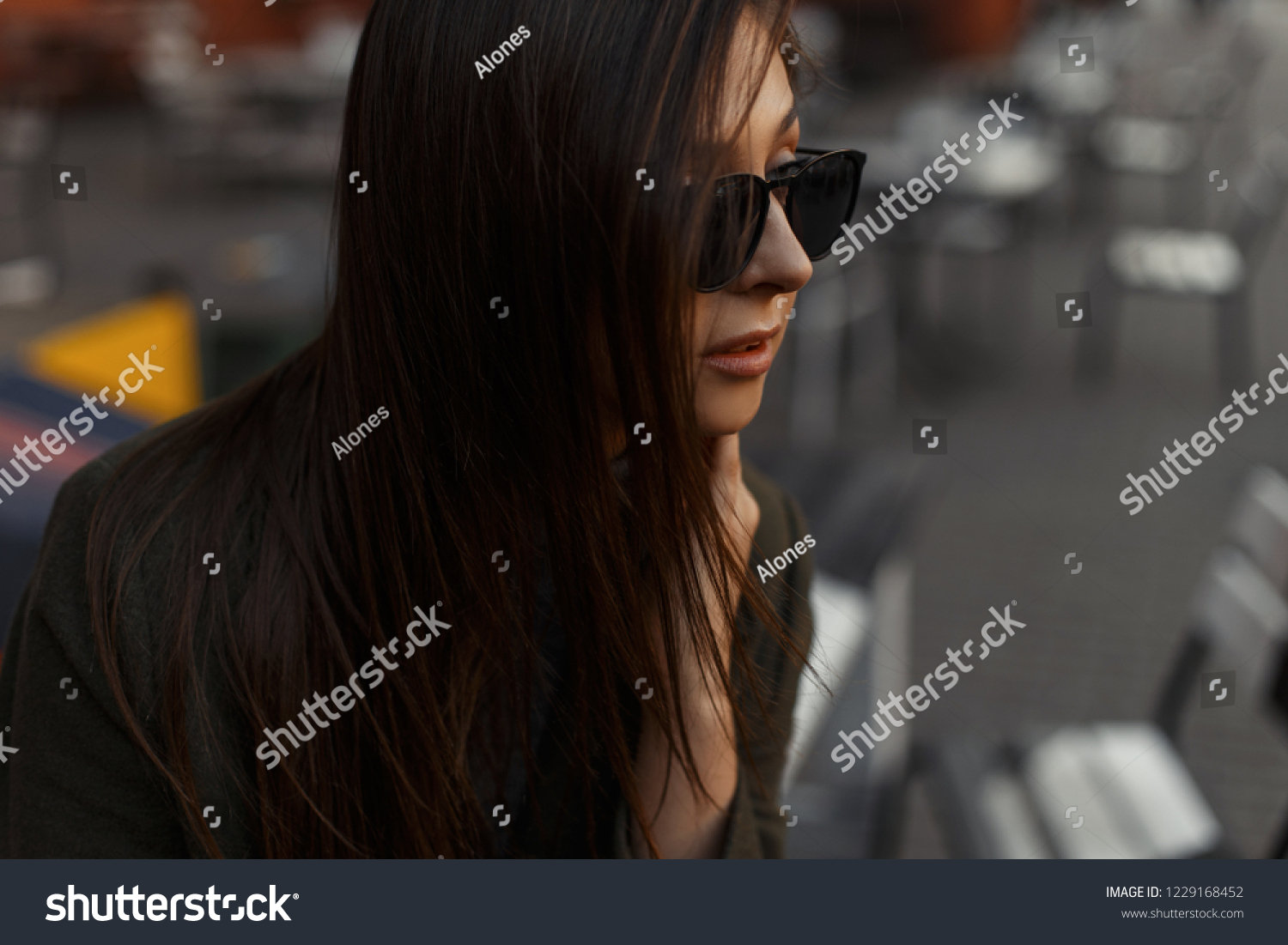 Portrait of a young stylish brunette woman sitting in an outdoor cafe in fashionable black sunglasses. #1229168452