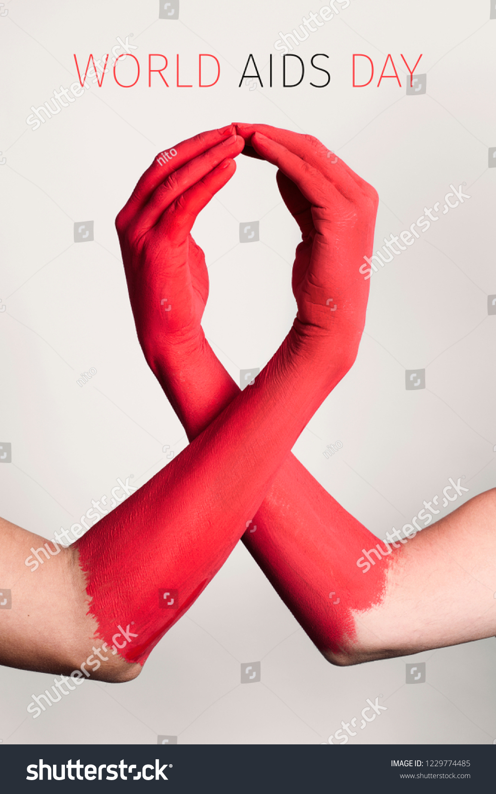 closeup of the arms of two men painted red forming a red awareness ribbon and the text world aids day against an off-white background #1229774485