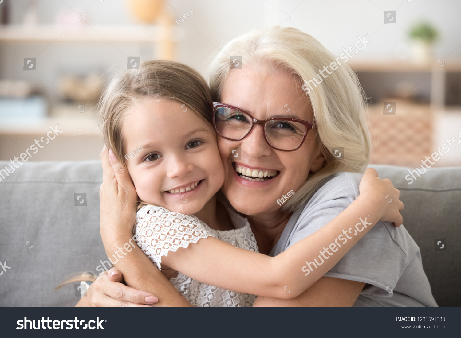 Happy old grandmother hugging little grandchild girl looking at camera, smiling mature mother or senior grandma granny laughing embracing adopted kid granddaughter sitting on couch, headshot portrait #1231591330