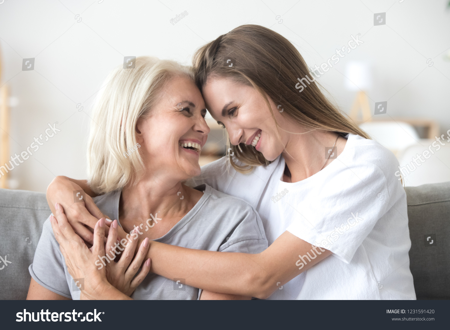 Happy loving older mature mother and grown millennial daughter laughing embracing, caring smiling young woman embracing happy senior middle aged mom having fun at home spending time together #1231591420