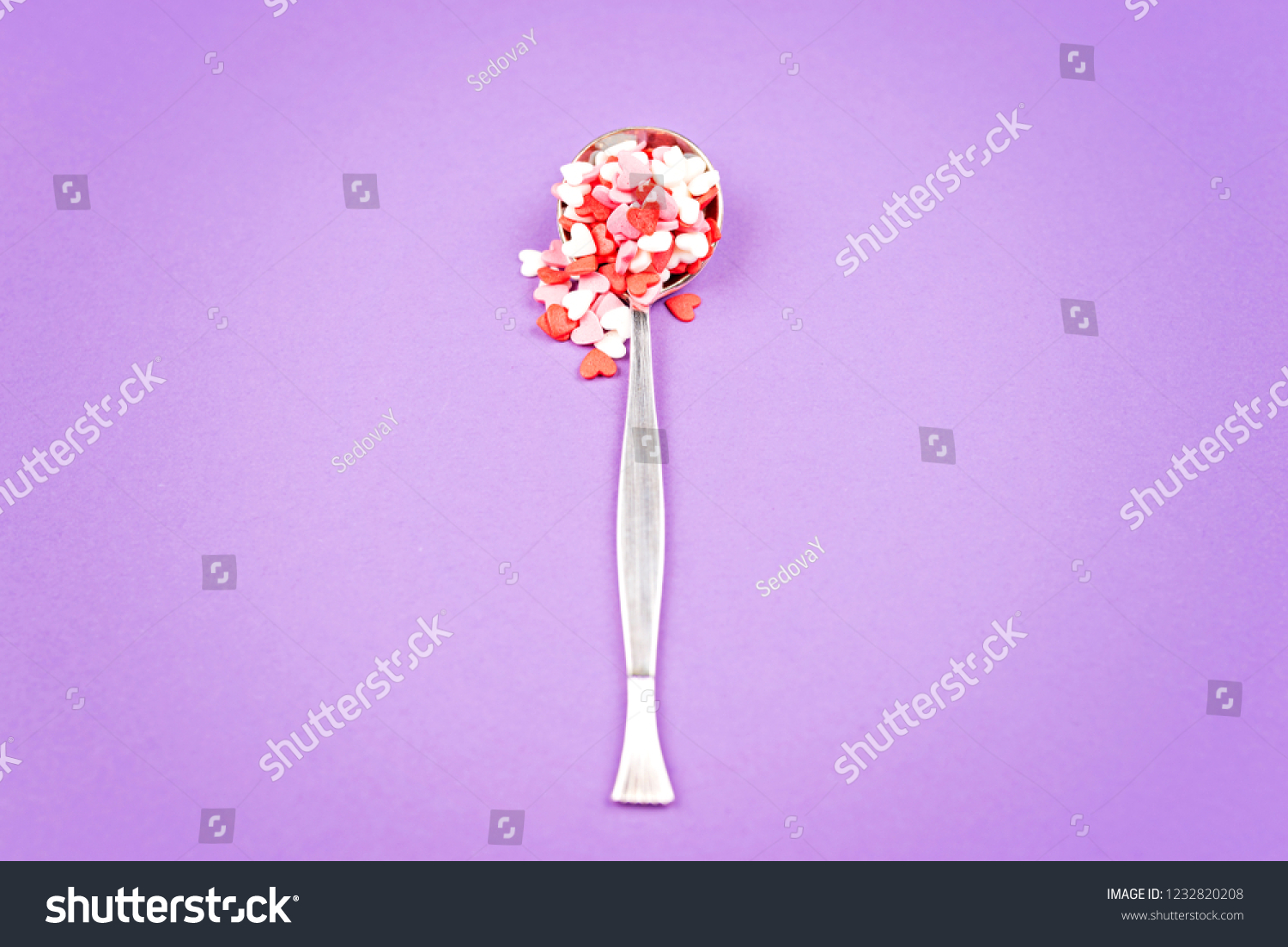 Vintage spoon with small pink, white, red sweet hearts on pastel Violet background. Flat lay stale. Valentine's Day celebration concept. Romantic mood. #1232820208