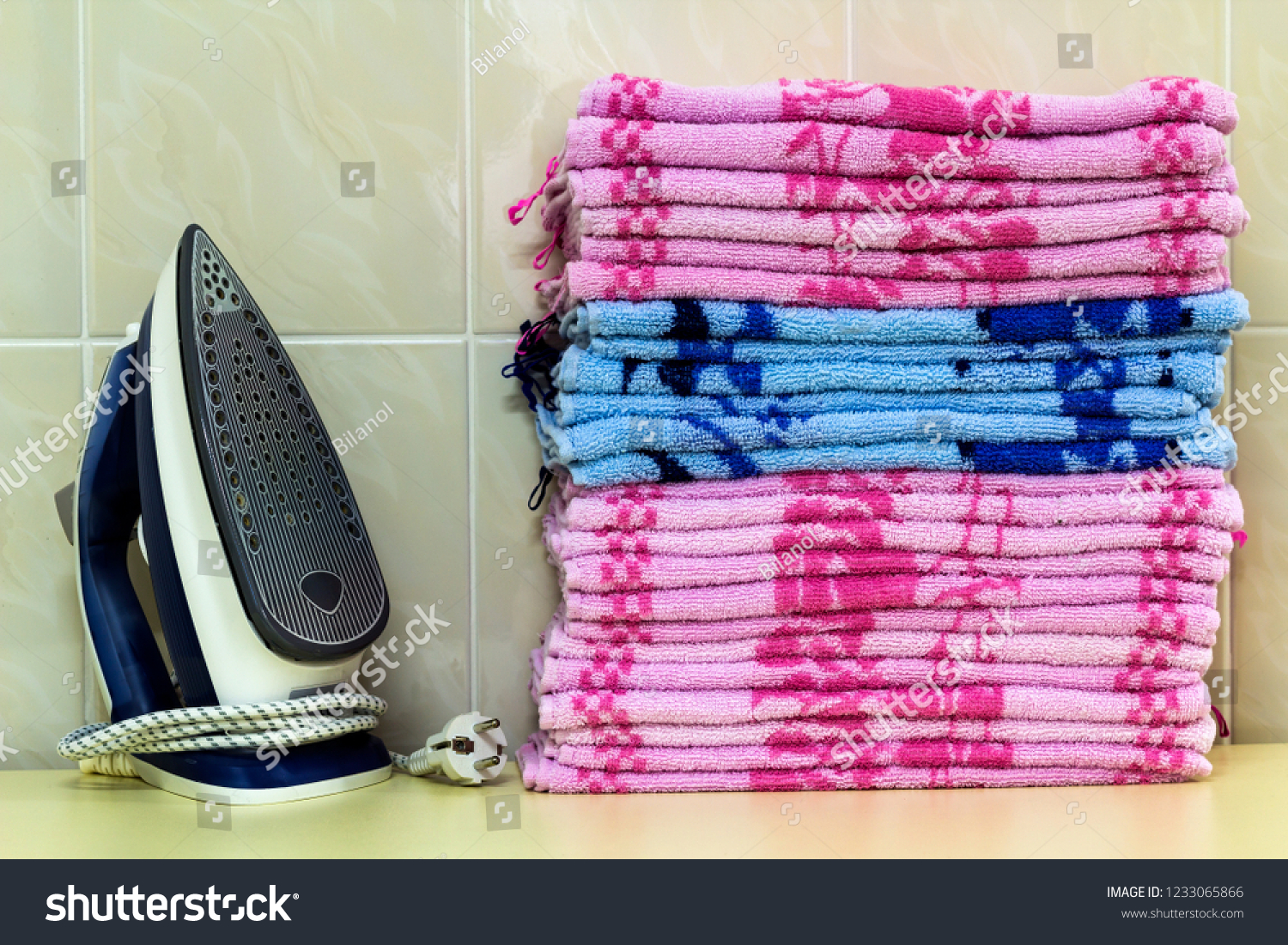Ironing linen with steam generator. A stack of ironed towels lying next to the iron. Teflon sole plate covered with small holes. #1233065866