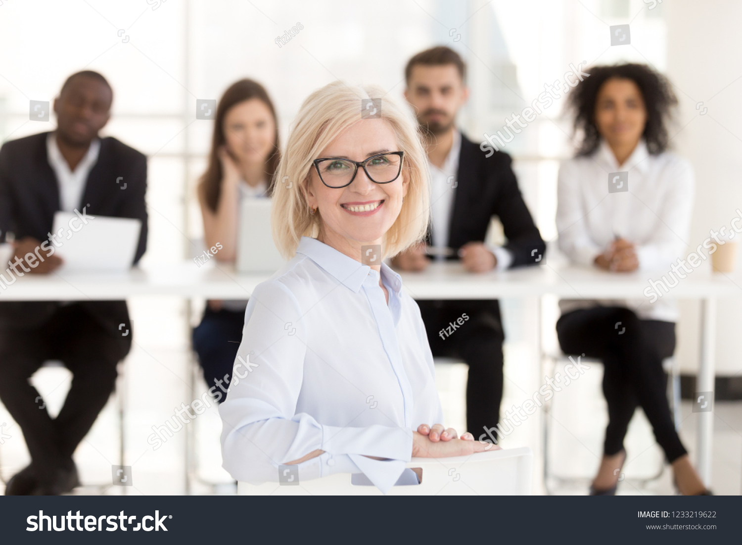 Smiling senior mature woman job applicant looks at camera at interview with hr recruiting team, happy middle aged lady business coach or vacancy candidate portrait, getting hired, employment concept #1233219622