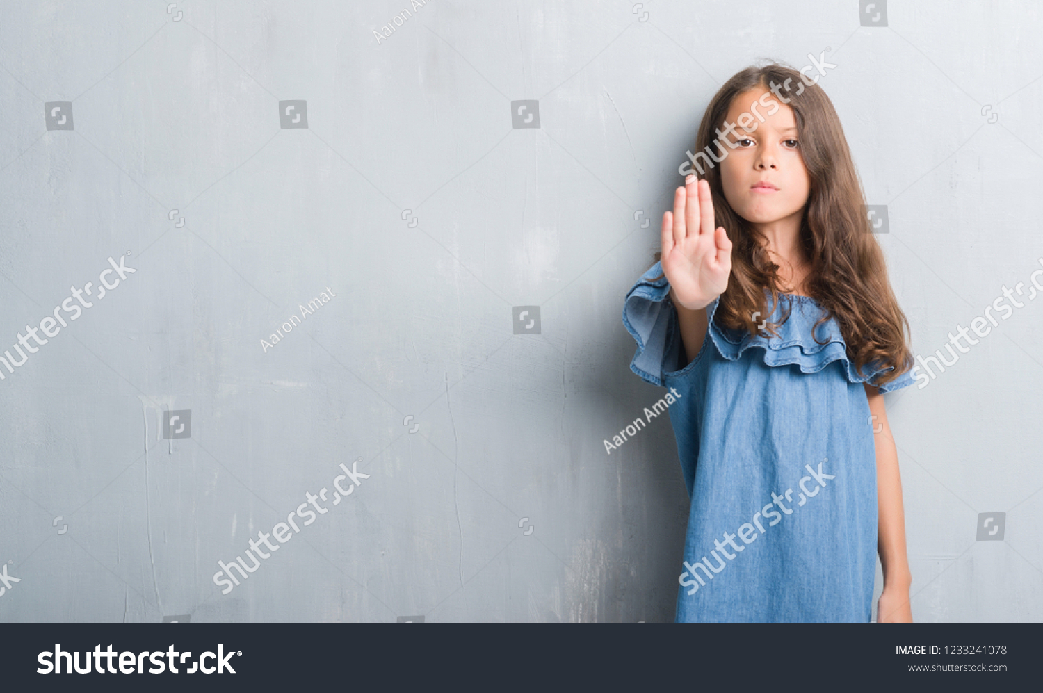 Young hispanic kid over grunge grey wall doing stop sing with palm of the hand. Warning expression with negative and serious gesture on the face. #1233241078