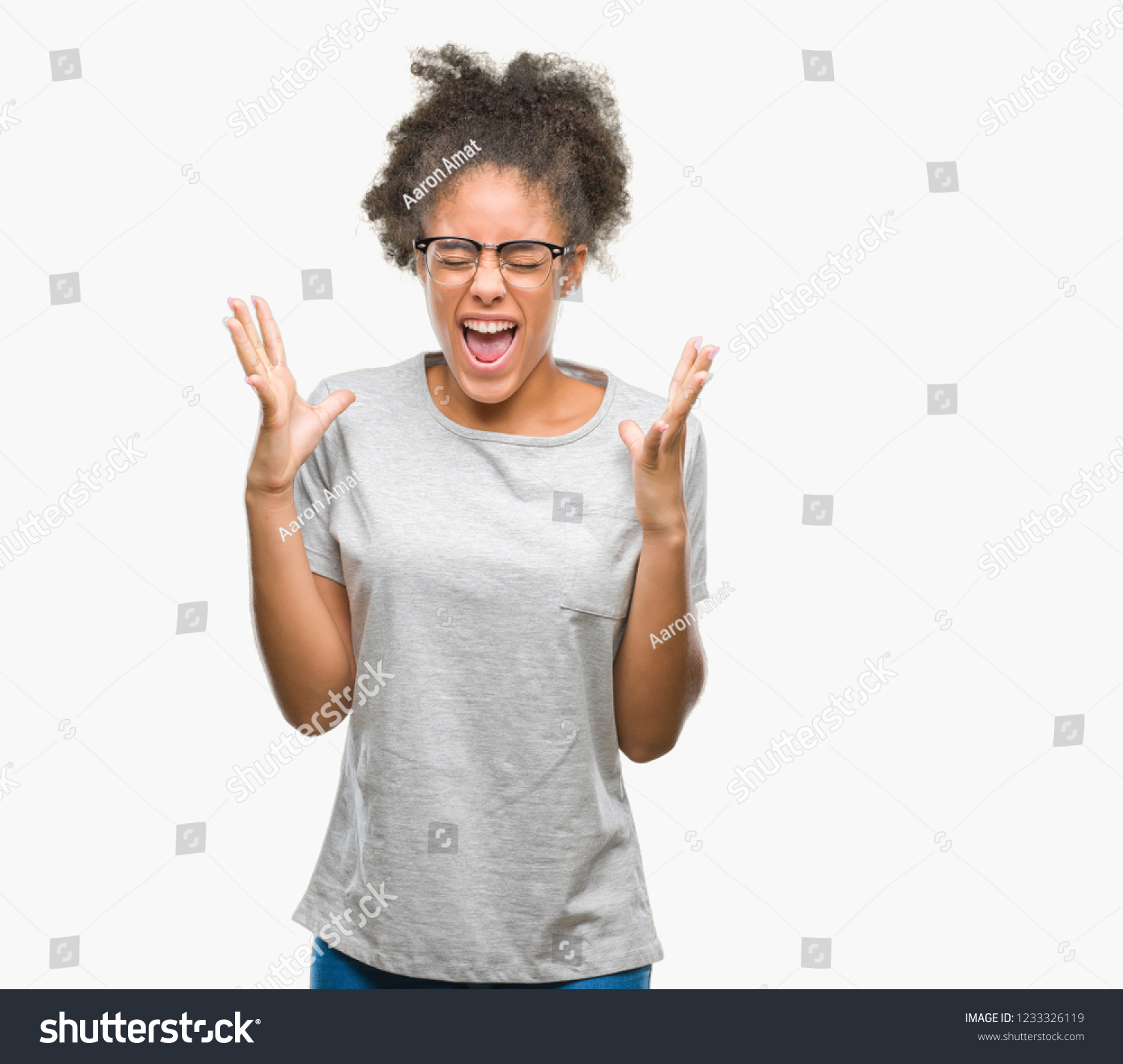 Young afro american woman wearing glasses over isolated background celebrating mad and crazy for success with arms raised and closed eyes screaming excited. Winner concept #1233326119