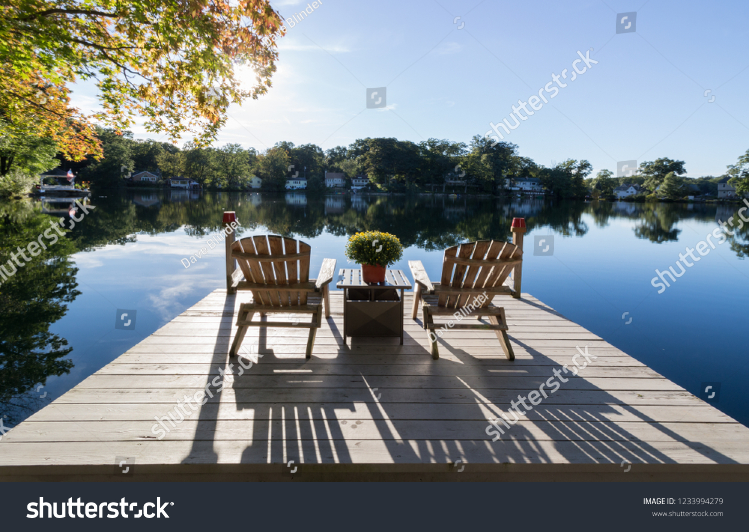 View of chairs and dock on a pristine lake with reflections and shadows #1233994279