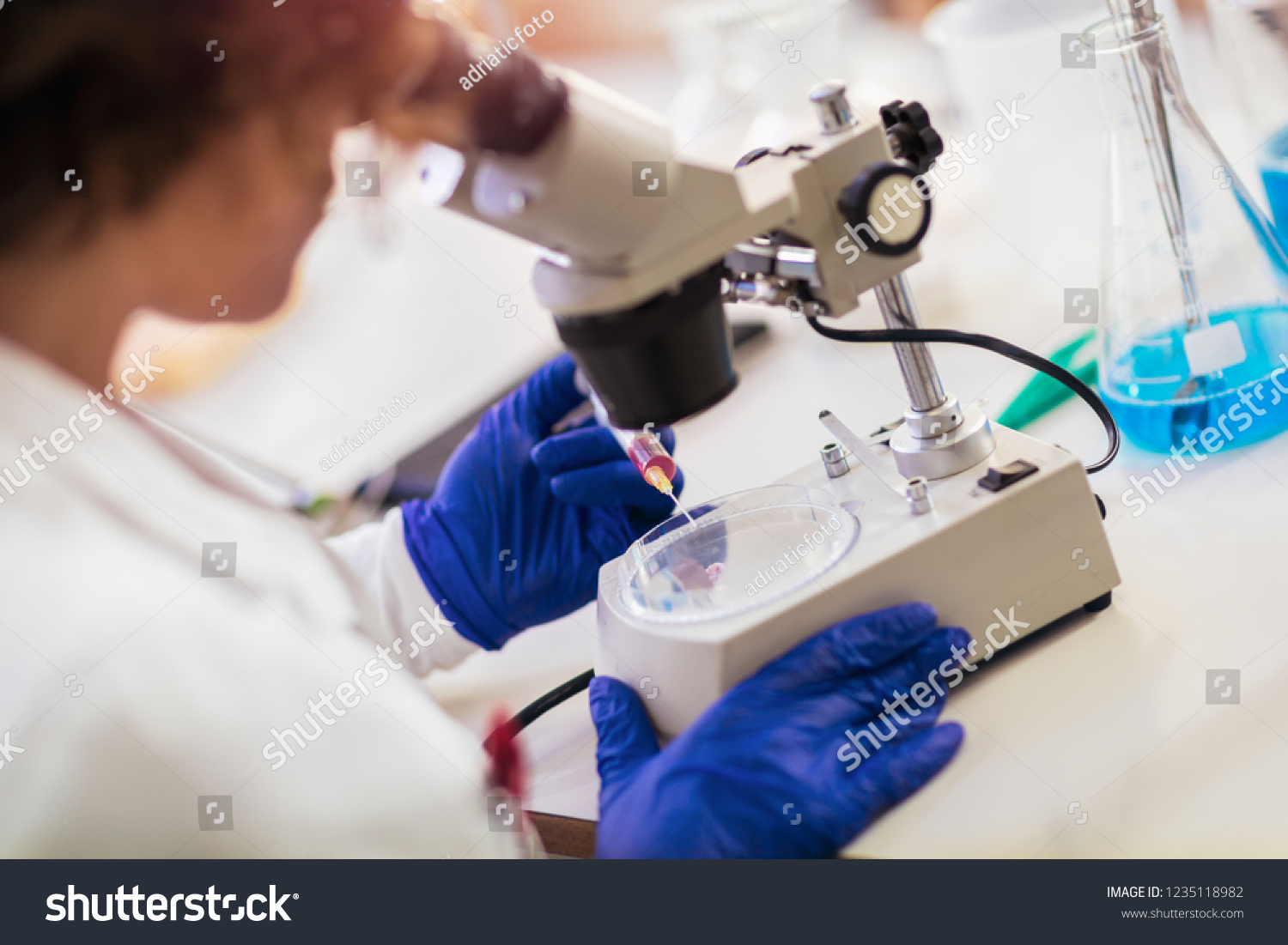Woman scienist in laboratory. Young scientist looking through a microscope in a laboratory. Young scientist doing some research. #1235118982