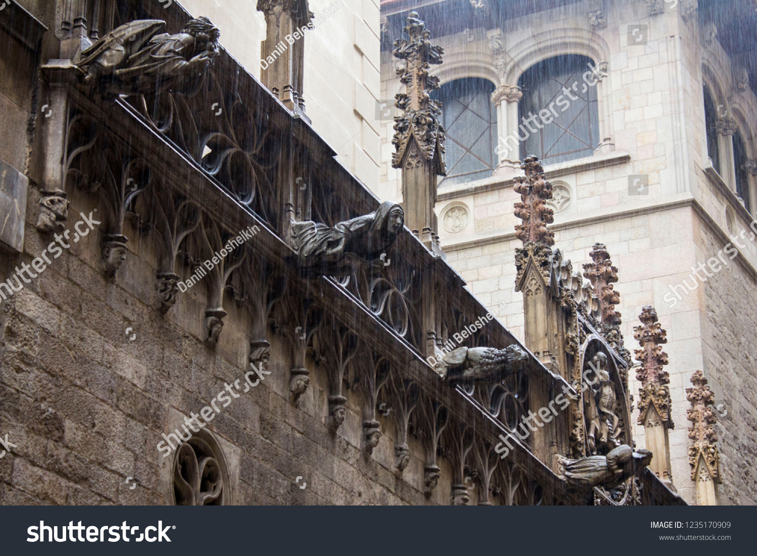 Cathedral various ancient gargoyles on the facade of old spanish gothic catholic cathedral under heavy rain in Barcelona, Spain. #1235170909