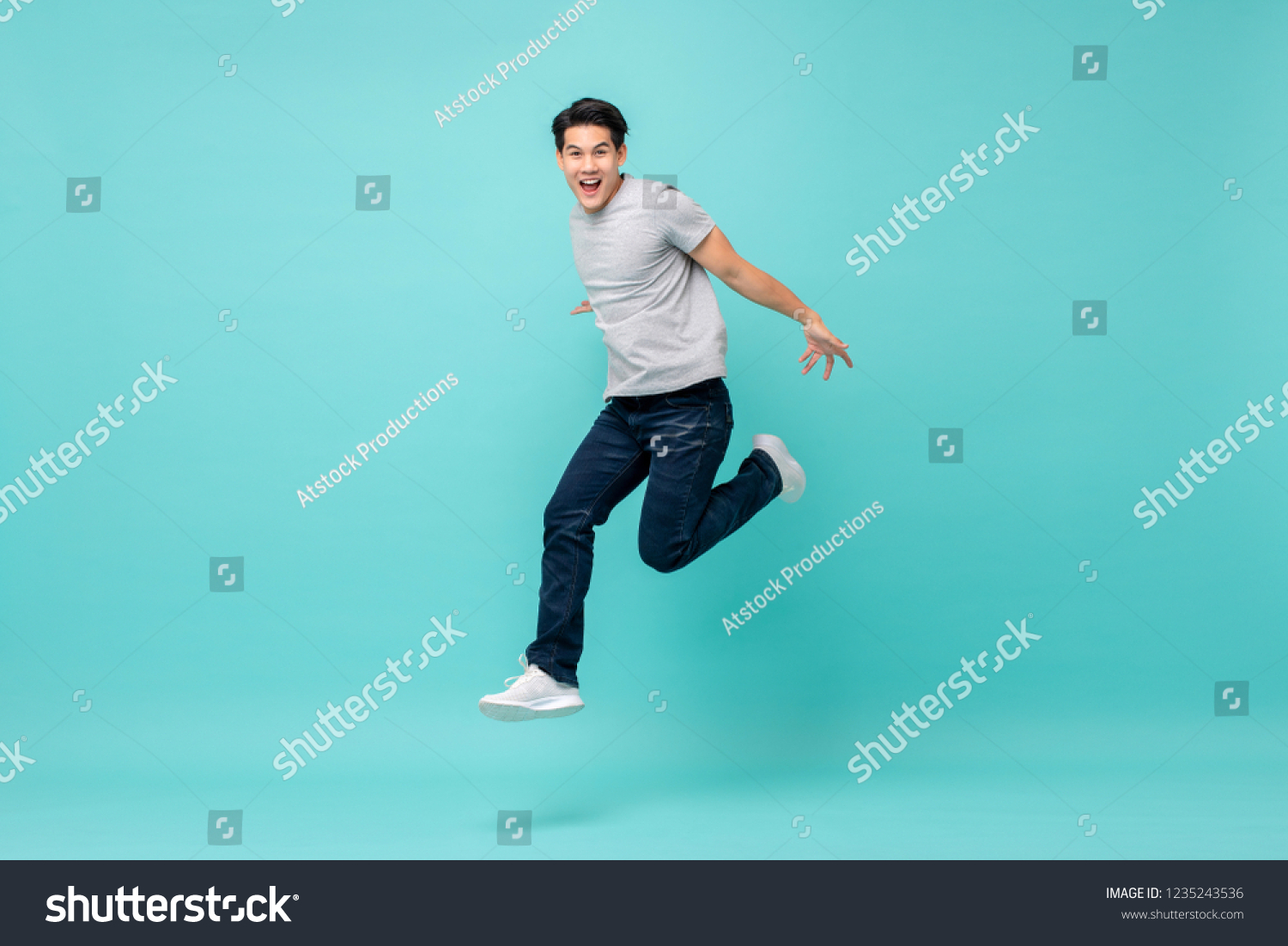 Energetic happy young Asian man in casual clothes jumping, studio shot isolated in light blue background #1235243536