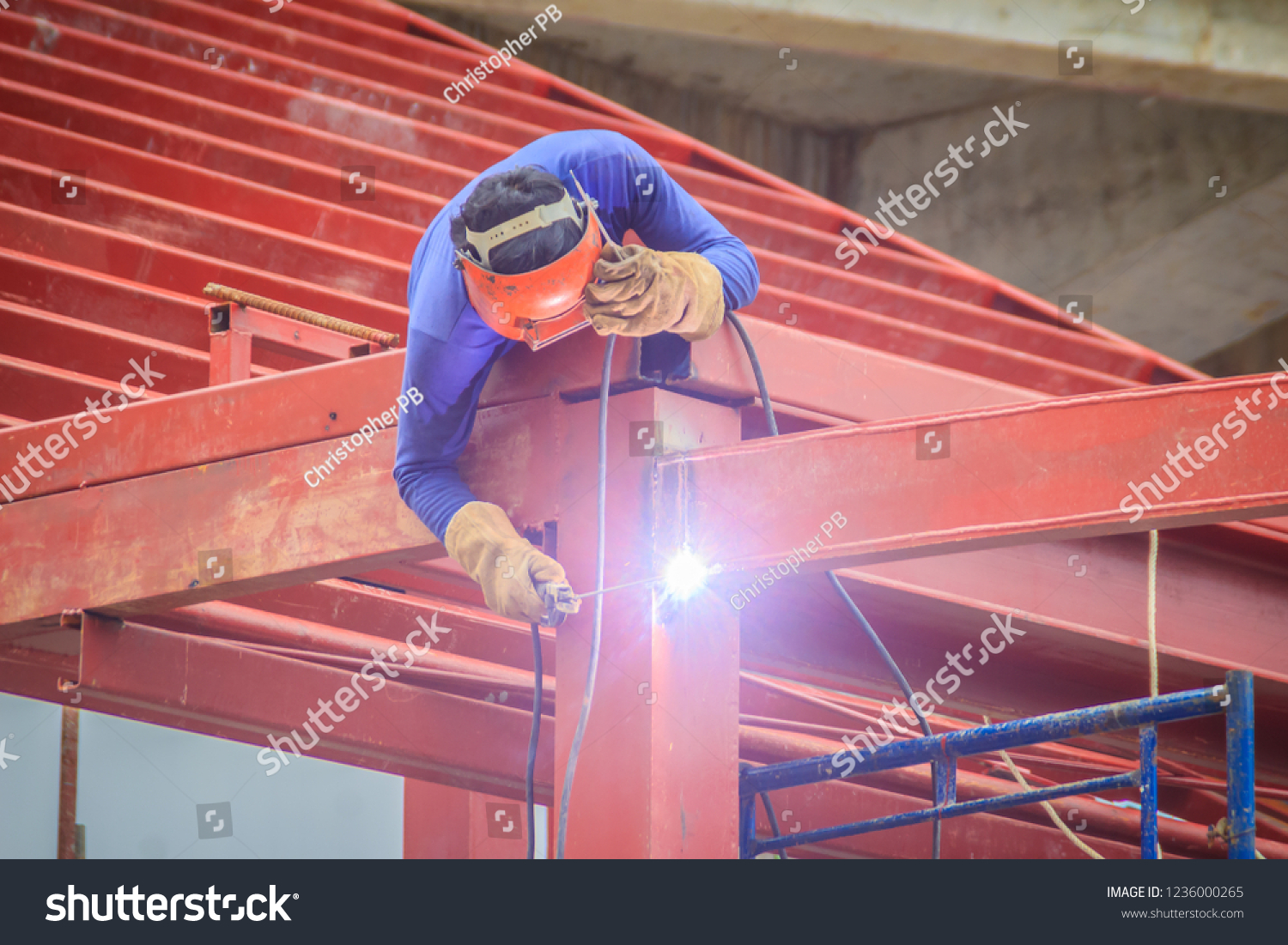 Risky welder while climbing and welding on top of the steel roof structure work at the building construction site. Skilled worker is welding on the high steel structure at the construction project. #1236000265