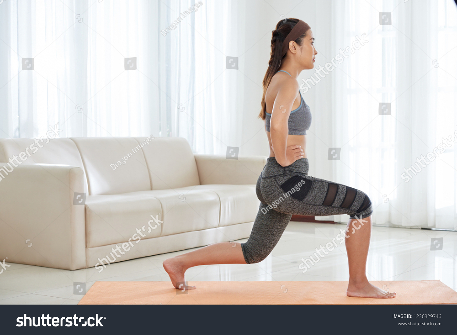 Side view of young athletic Asian woman in activewear doing lunge exercise while having workout at home #1236329746