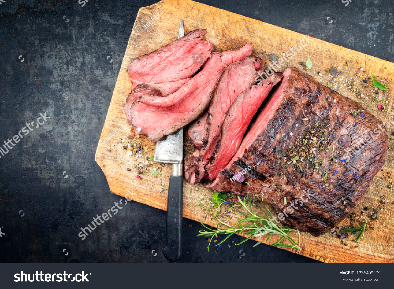 Traditional barbecue dry aged sliced roast beef steak with herbs as top view on an old cutting board with copy space left #1236408979