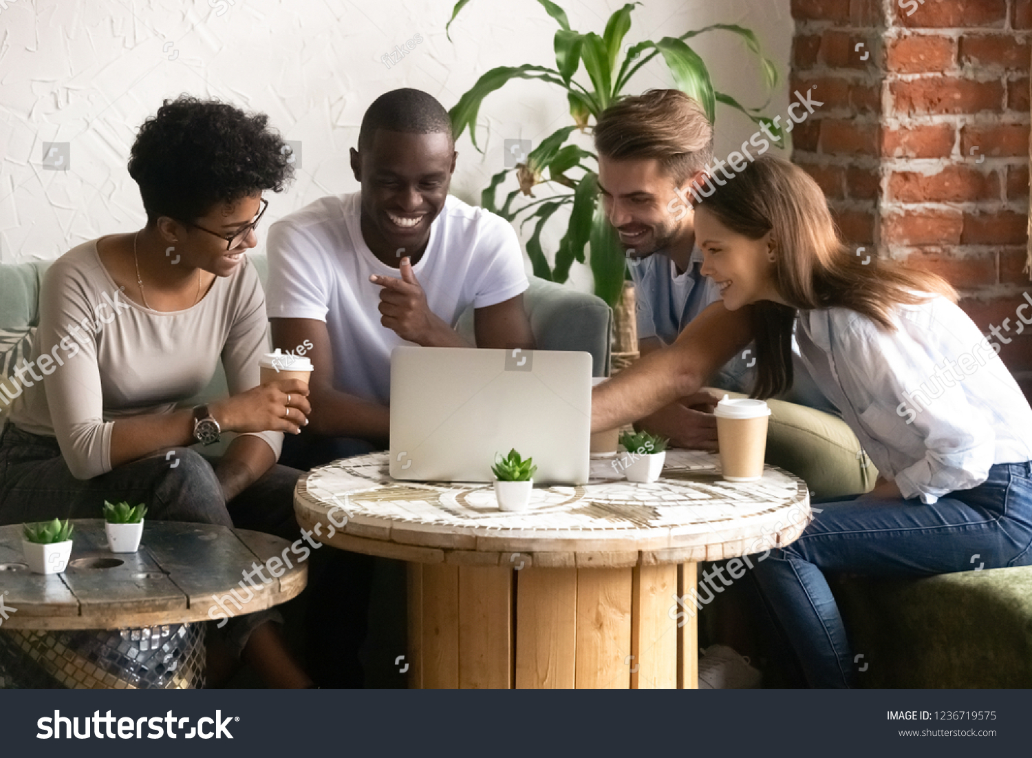 Happy smiling diverse friends using laptop together in cafe, watching funny video online, comedy movie during lunch in coffee house, multiracial people having fun together, free time activities #1236719575