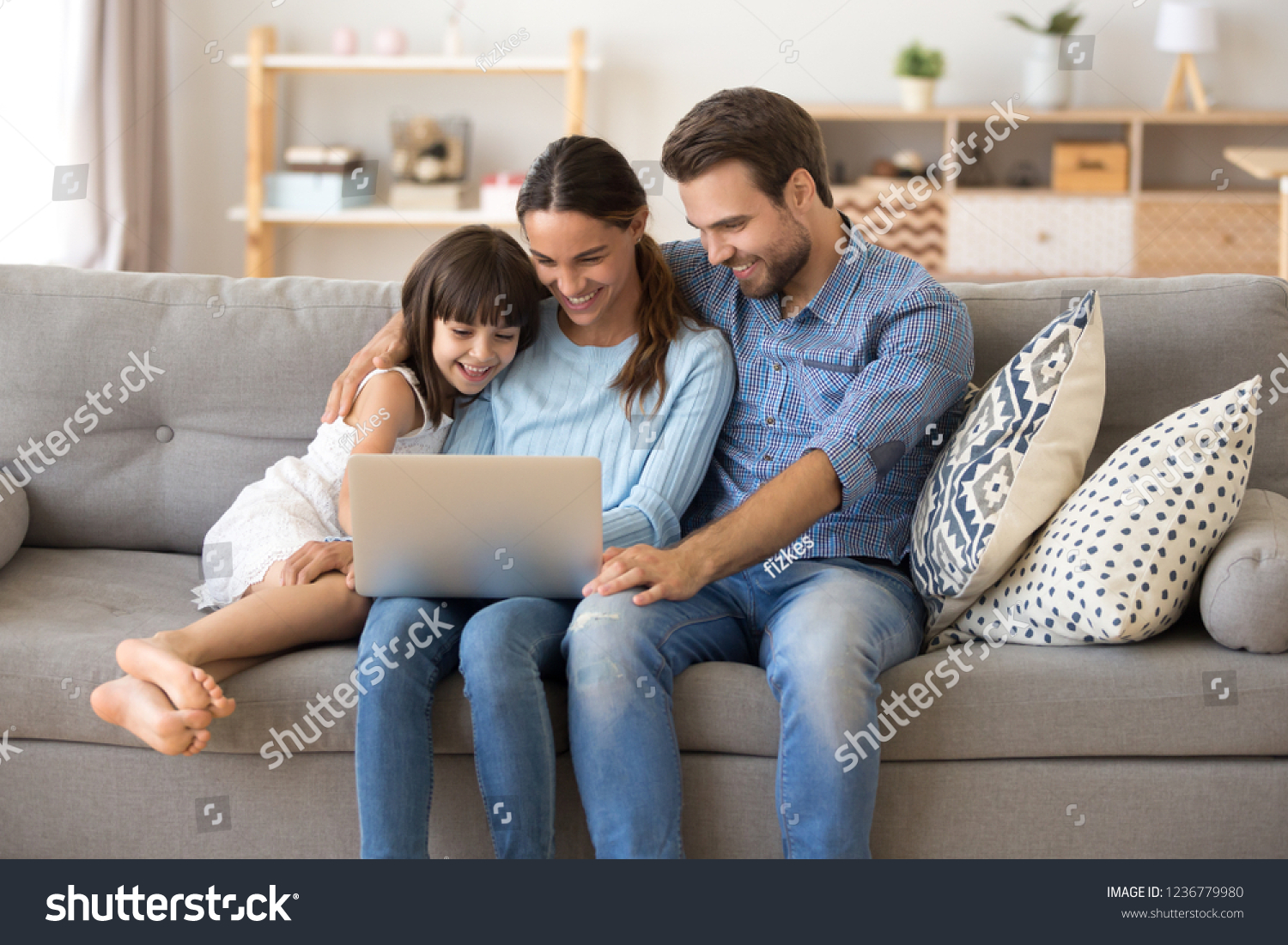 Married diverse couple and little preschool daughter sitting on couch using computer watching movie cartoons online surfing internet shopping purchasing via internet spending weekend together at home #1236779980