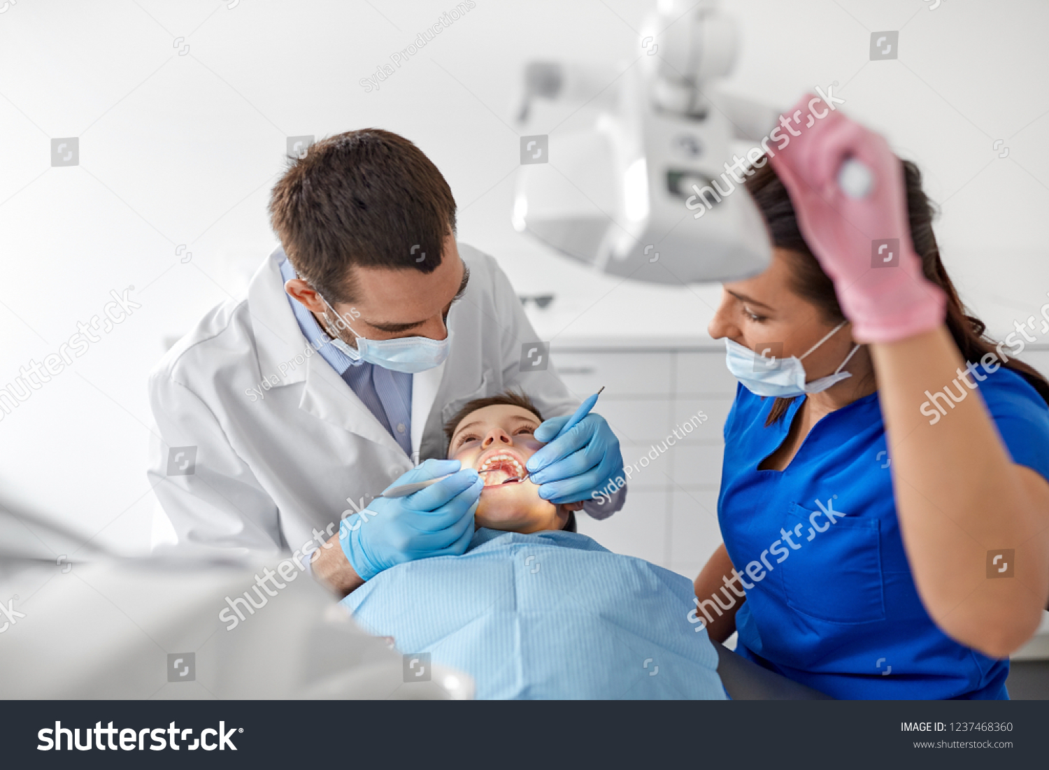 medicine, dentistry and healthcare concept - dentist with mouth mirror and probe checking for kid patient teeth at dental clinic #1237468360