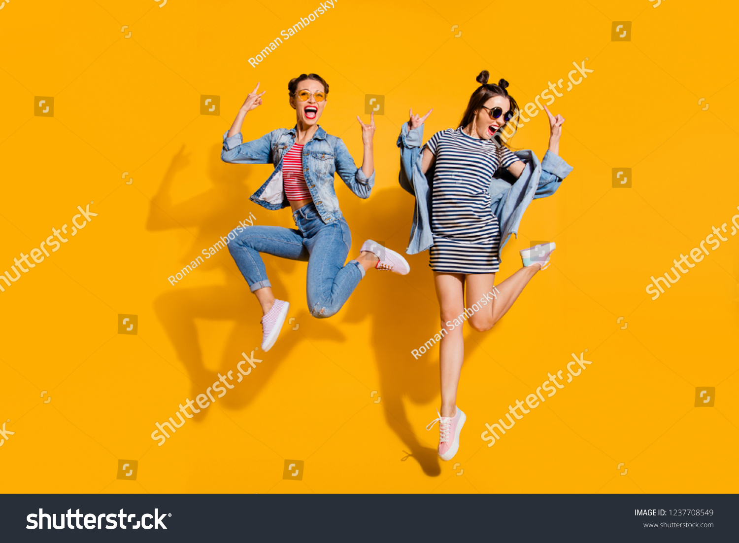 Full legs body size two music lover lady with emotion reaction facial expression wear in glasses spectacles street style stylish trendy casual outfit isolated on yellow wall give heavy metal gesture #1237708549