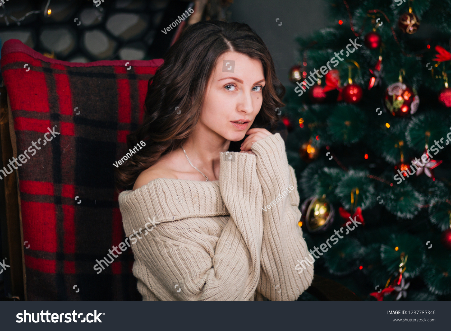 Beautiful young girl in a New Year's interior. A woman is sitting near the fireplace in a rocking chair. New Year. Christmas mood #1237785346
