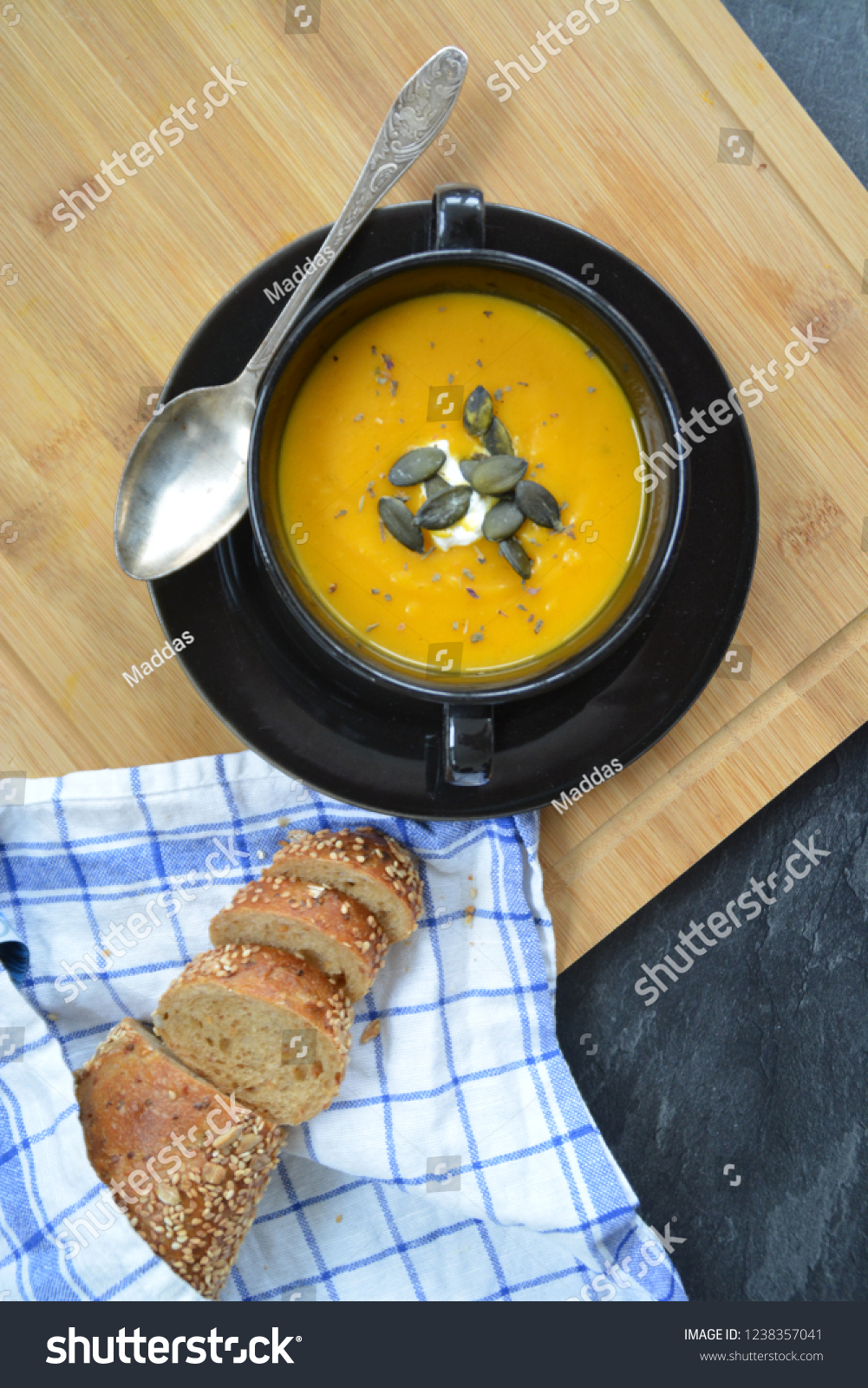 Pumpkin cream soup in a small bowl and on a wooden board on a kitchen surface with a whole pumpkin and sliced ​​bread beside it - autumnal feasting #1238357041