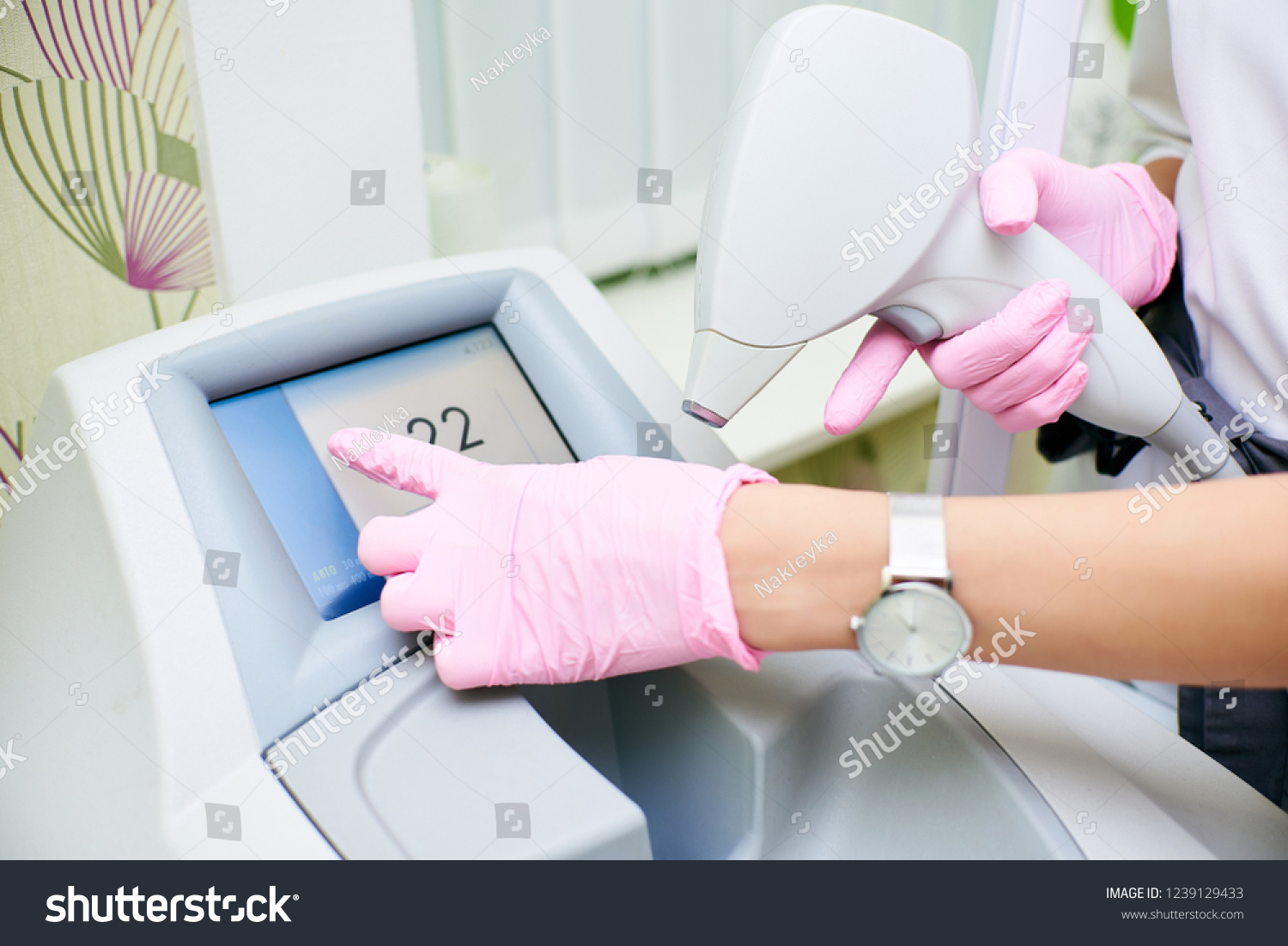 Hands of the doctor in pink gloves hold the device for an epilation and press the touch screen. The concept of control device, laser hair removal #1239129433