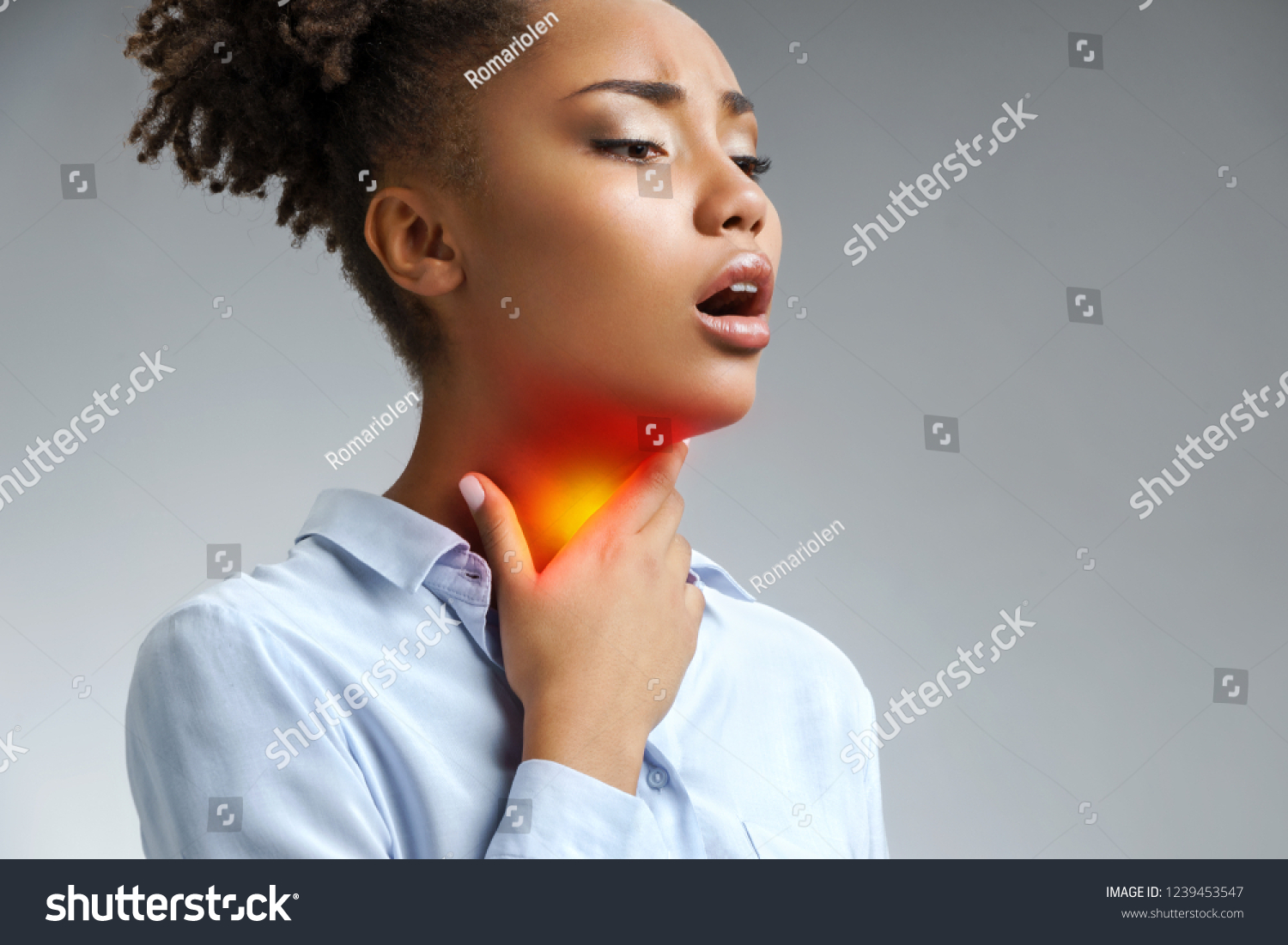 Throat pain. Woman holding her inflamed throat. Photo of african american woman in blue shirt on gray background. Medical concept #1239453547