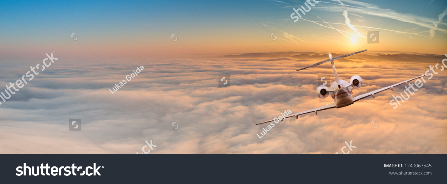 Panorama view of private jet plane flying above dramatic clouds during sunset. #1240067545