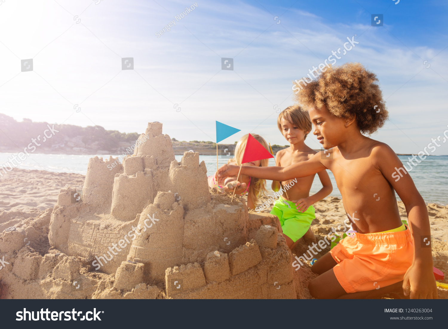 Happy kids decorating sandcastle towers with flags #1240263004