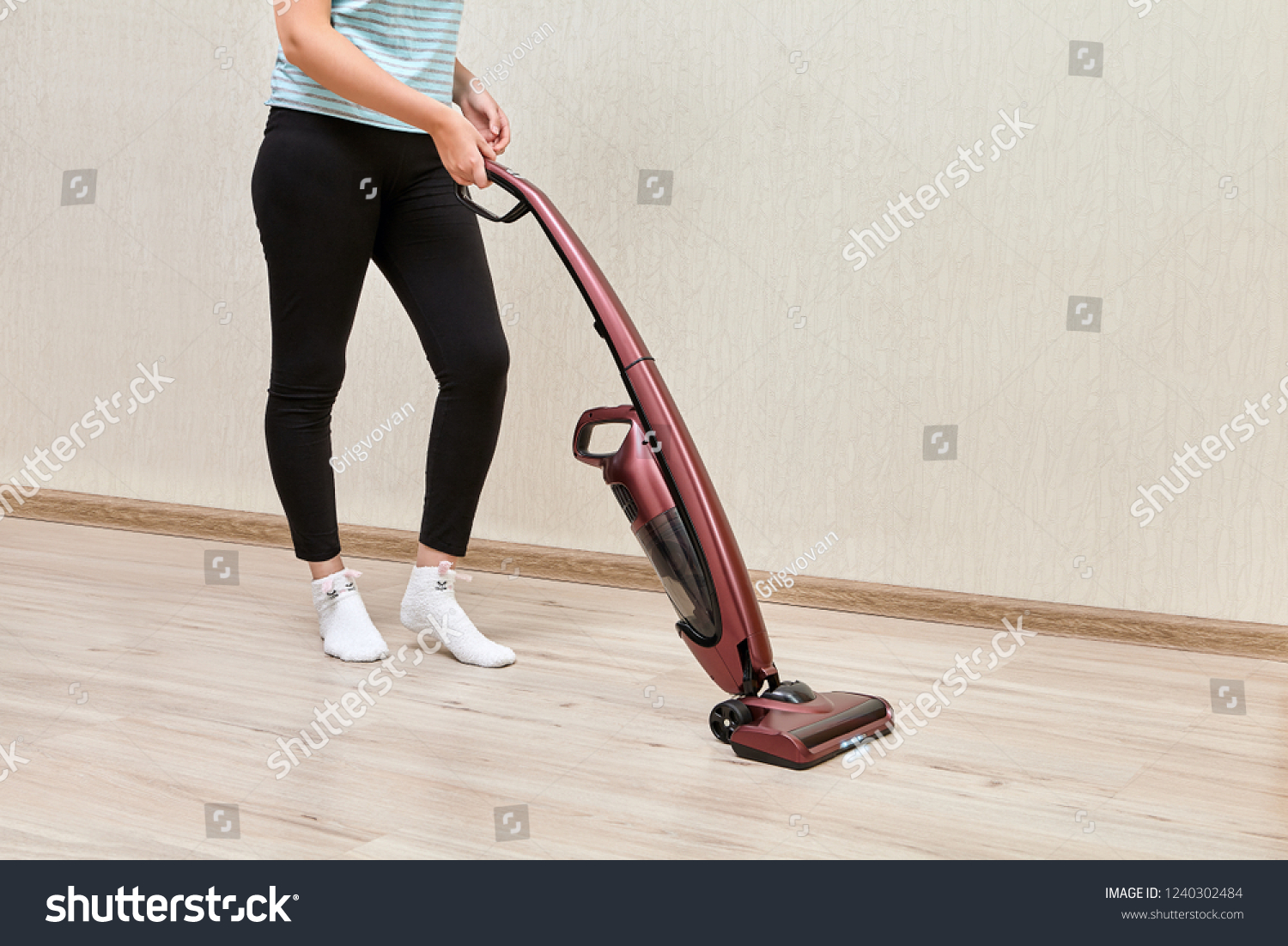 Cleaning woman in black leggins is vacuuming with help of upright vacuum cleaner with led lights on. #1240302484