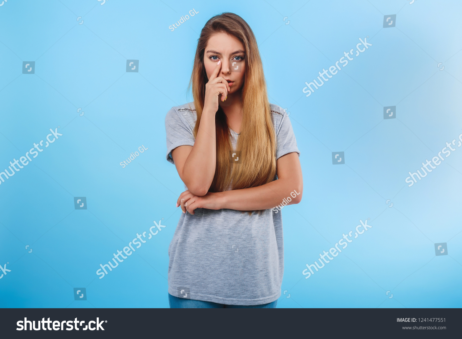 Distressed girl on blue background touches her nose intently. Concept disease, malaise, problems. #1241477551