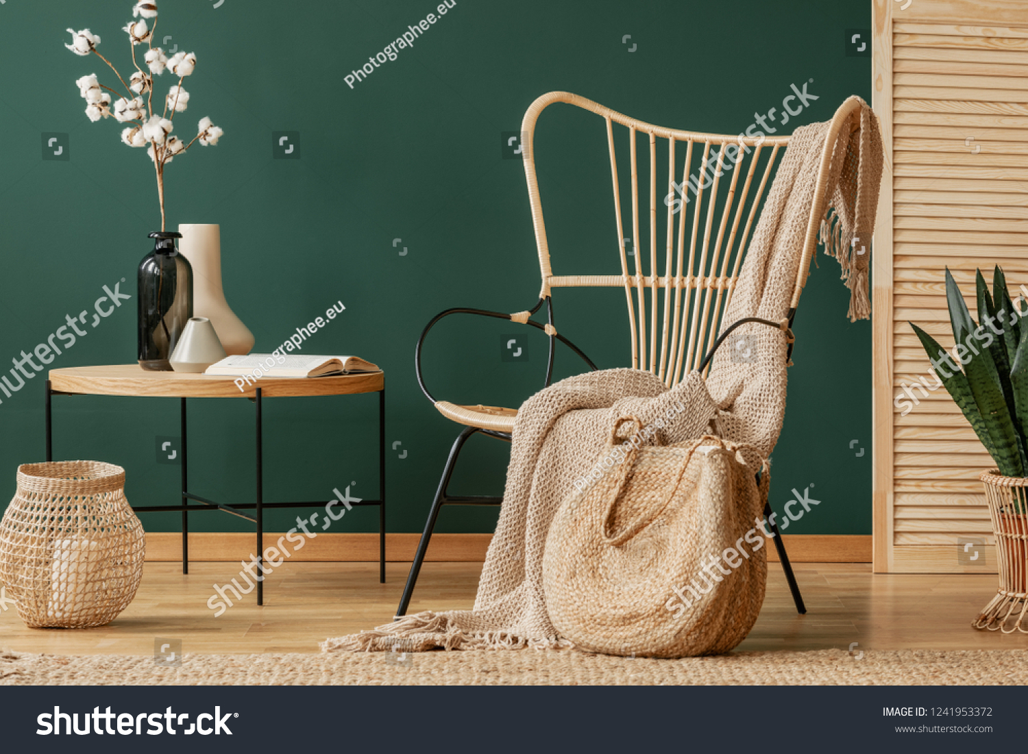 Blanket on rattan armchair next to table with flowers in green flat interior with lantern. Real photo #1241953372