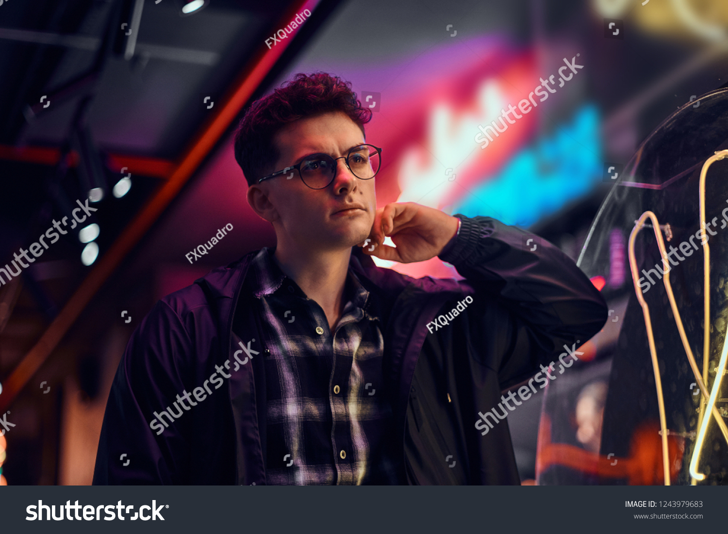 A handsome young man standing at night in the street. Illuminated signboards, neon, lights. #1243979683