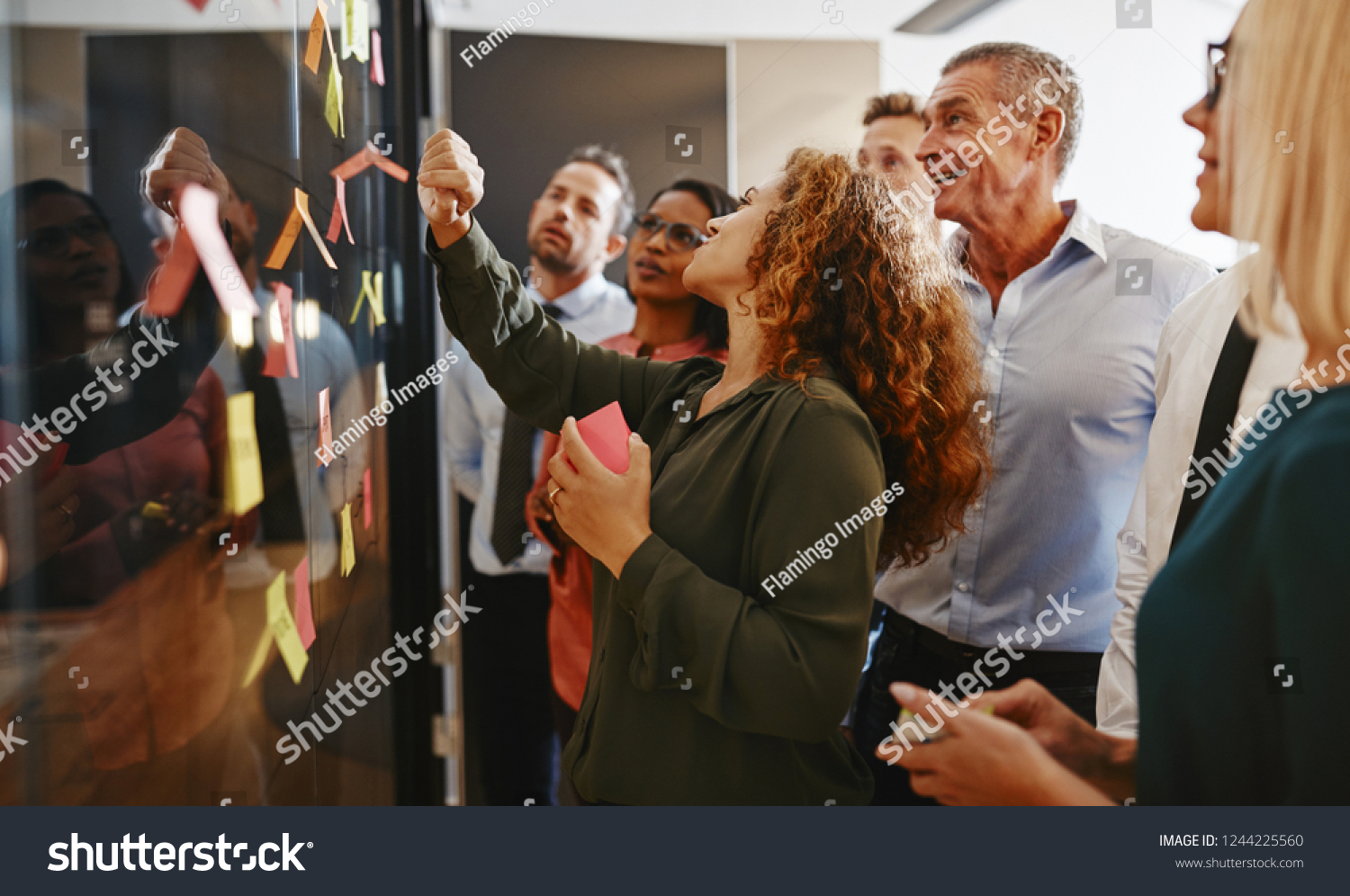 Group of diverse businesspeople strategizing with sticky notes on a glass wall while working together in a modern office #1244225560