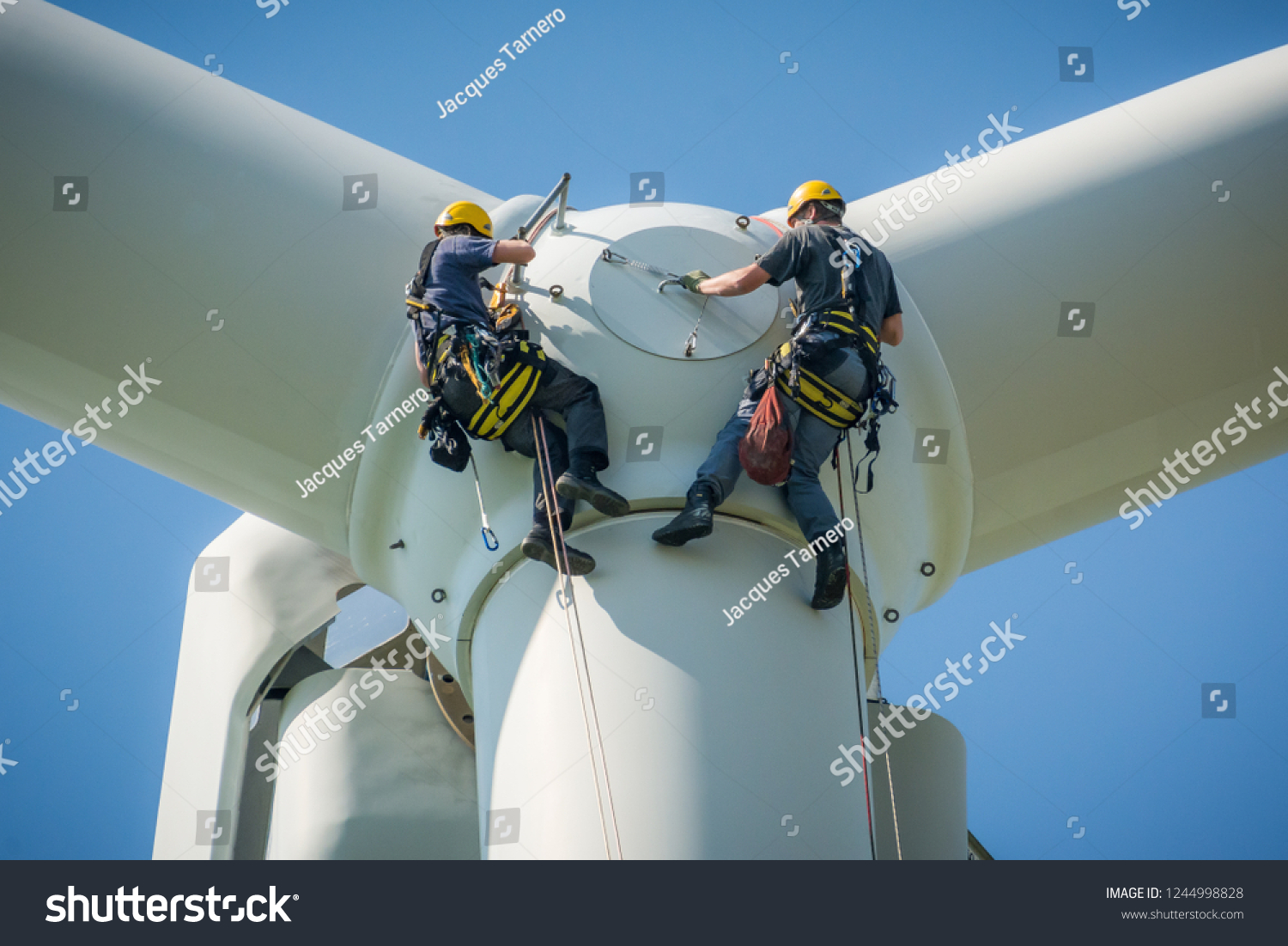 Inspection engineers preparing to rappel down a rotor blade of a wind turbine in a North German wind farm on a clear day with blue sky. #1244998828