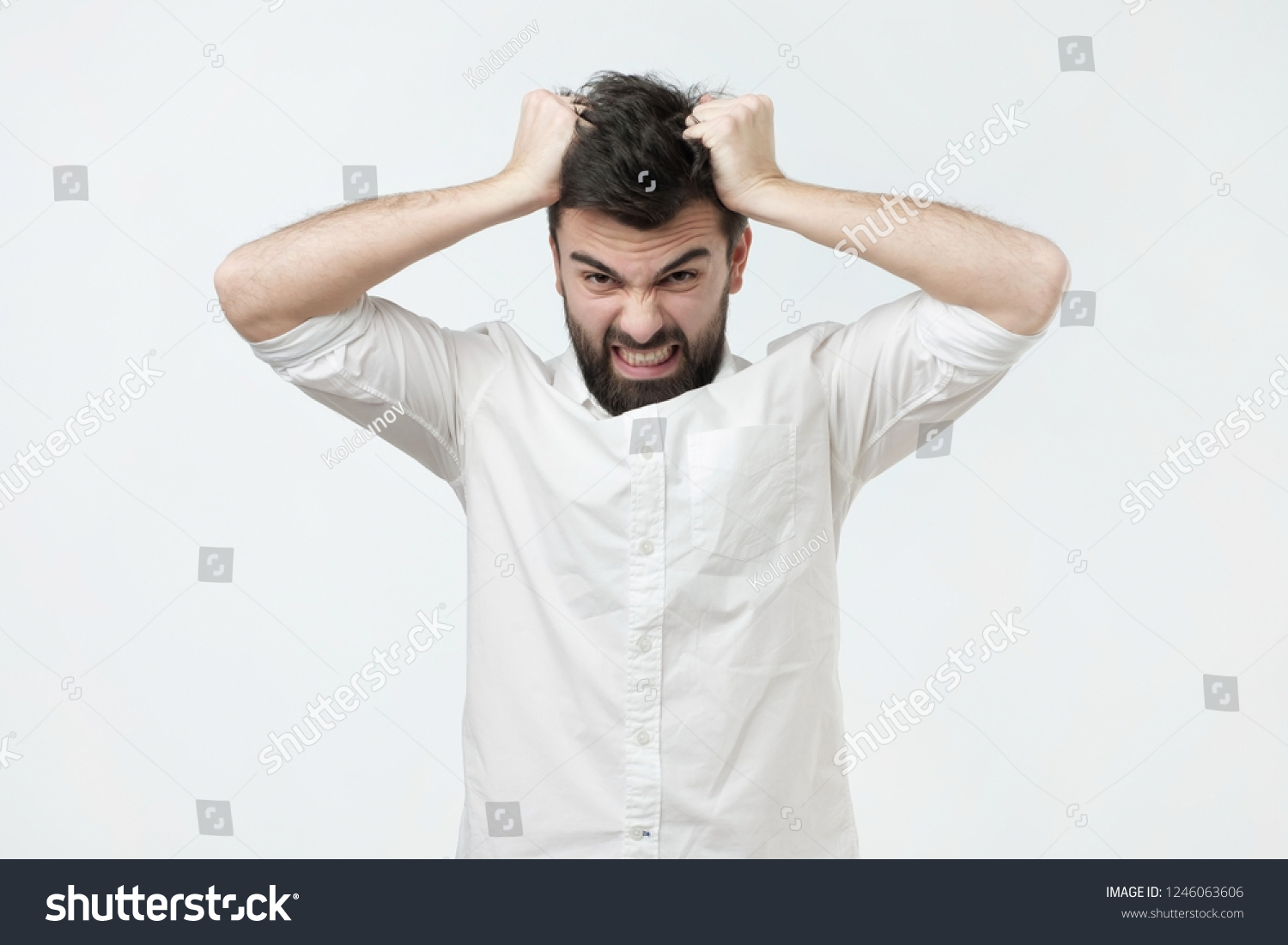 Angry and furious man on a gray background. He pulls out his hair in a rage #1246063606
