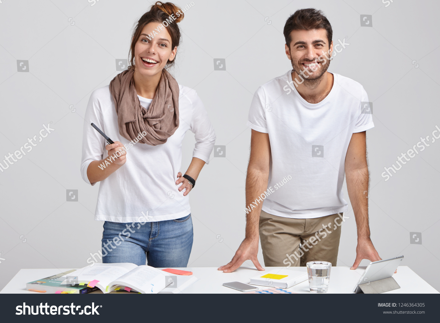 Photo of cheerful woman and man designers dressed in fashionable clothes, stand near white desk, study literature, make project work on tablet, connected to wireless internet. People and profession #1246364305