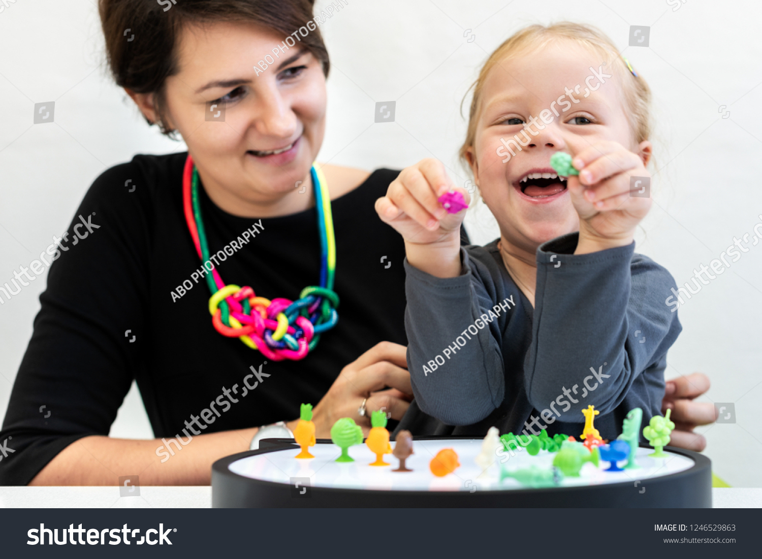 Toddler girl in child occupational therapy session doing sensory playful exercises with her therapist.  #1246529863