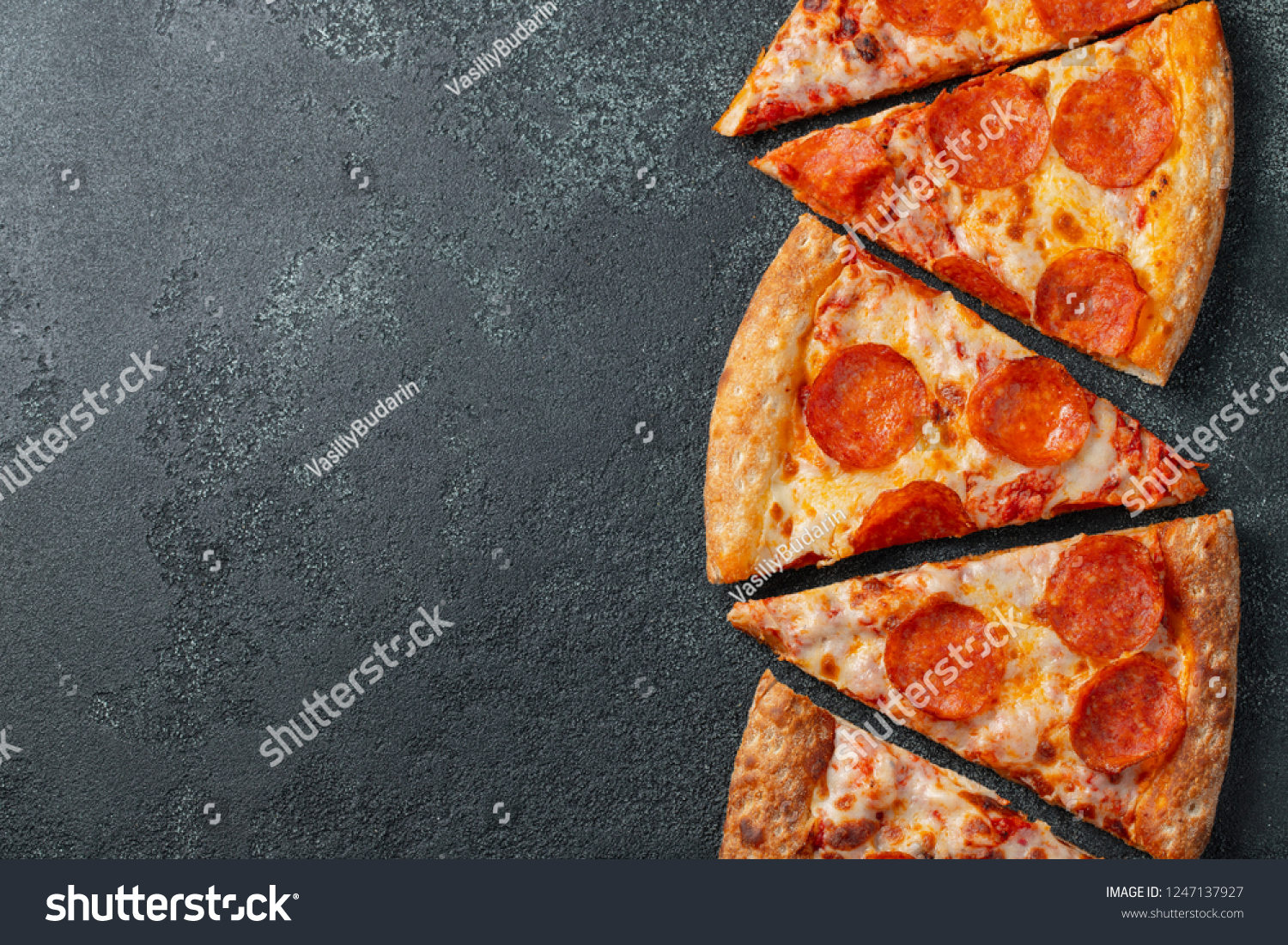 Cut into slices delicious fresh pizza with sausage pepperoni and cheese on a dark background. Top view with copy space for text. Pizza on the black concrete table. flat lay #1247137927