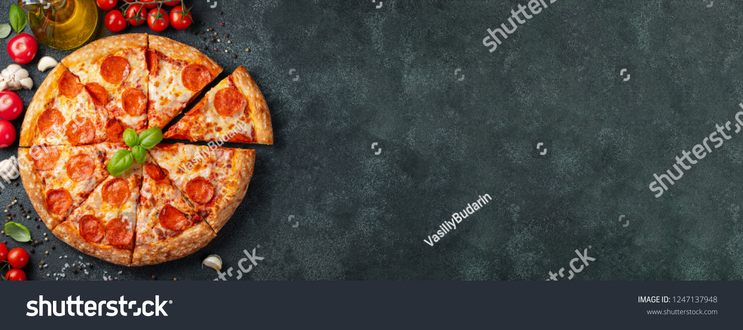 Tasty pepperoni pizza and cooking ingredients tomatoes basil on black concrete background. Top view of hot pepperoni pizza. With copy space for text. Flat lay. Banner #1247137948