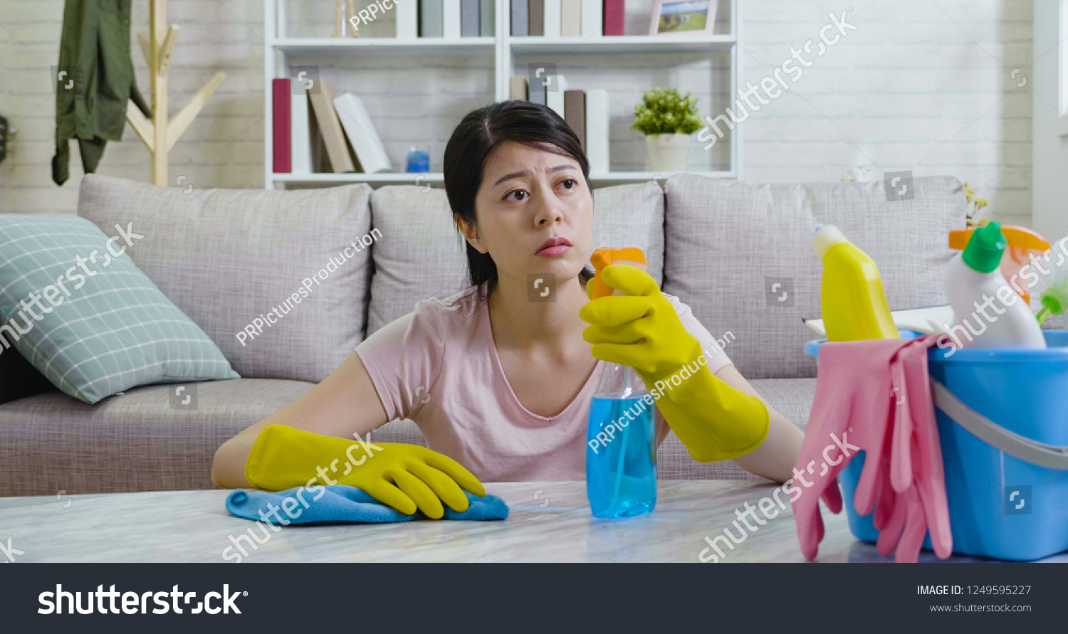 Exhausted asian housewife looking outside the house from window to the urban city view. young lady sitting on floor resting while doing housework wiping table. elegant woman wearing gloves cleaning. #1249595227
