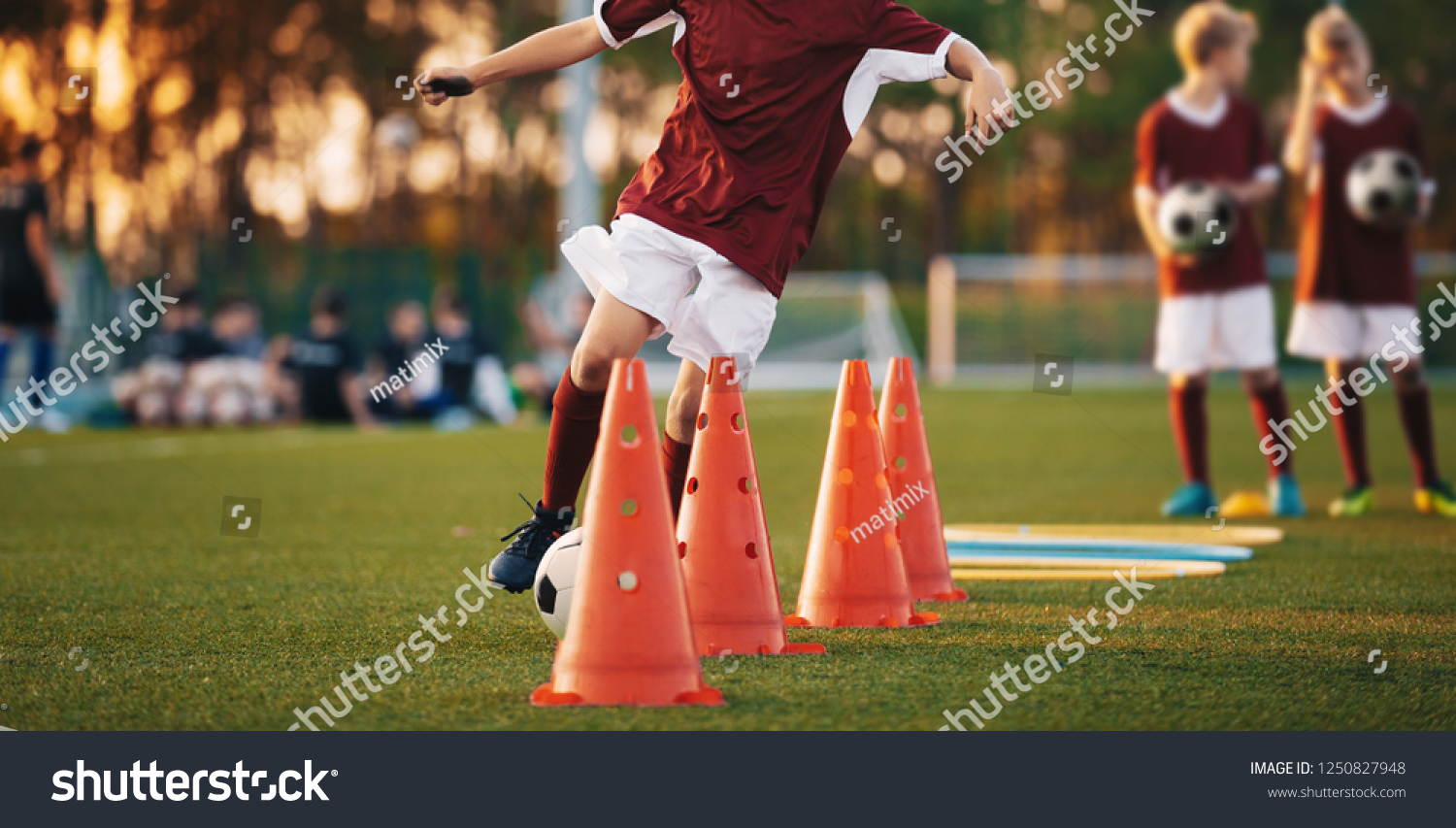 Football Drills: The Slalom Drill. Youth soccer practice drills. Young football players training on pitch. Soccer slalom cone drill. Boy in red soccer jersey shirt running with ball between cones #1250827948