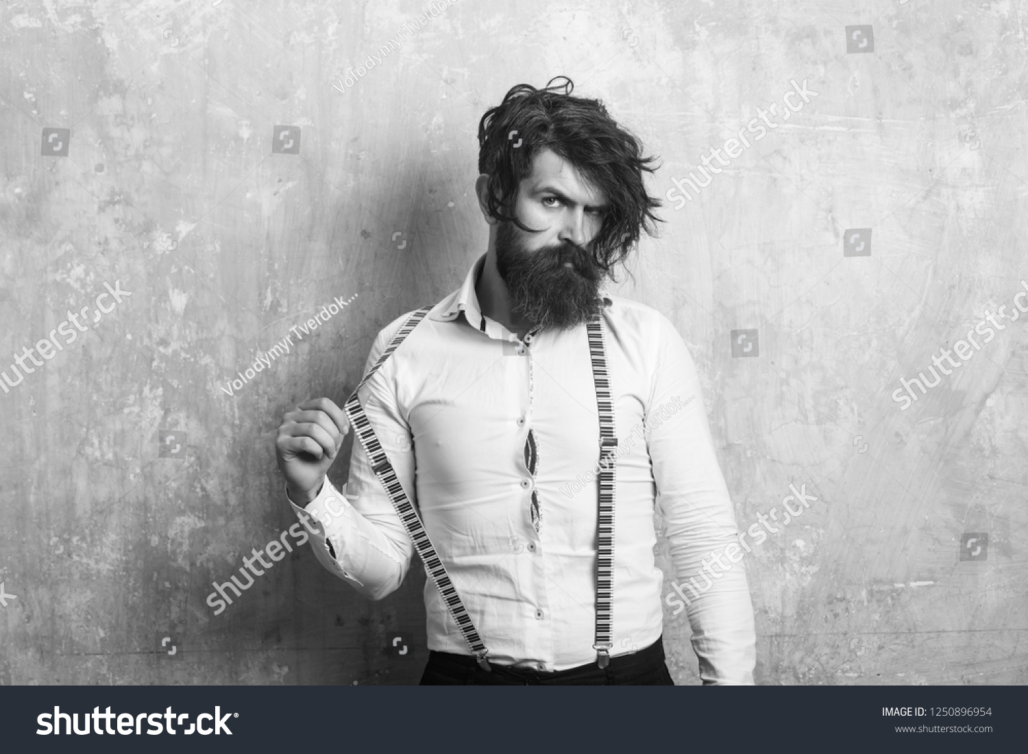 Business fashion and beauty. Fashion model with stylish hair. Guy or businessman at textured wall. Man with long beard and mustache on face. Hipster in shirt and suspenders. #1250896954