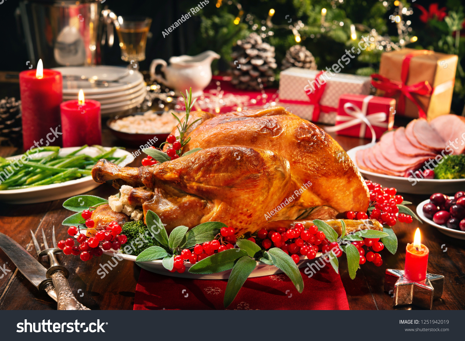 Christmas turkey dinner. Baked turkey garnished with red berries and sage leaves in front of Christmas tree and burning candles #1251942019