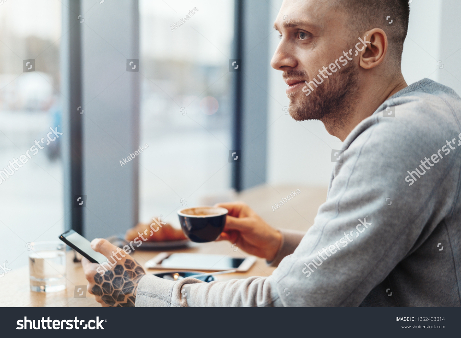 Close up of man with tattoo holding cup of coffee and mobile phone in cafe. #1252433014