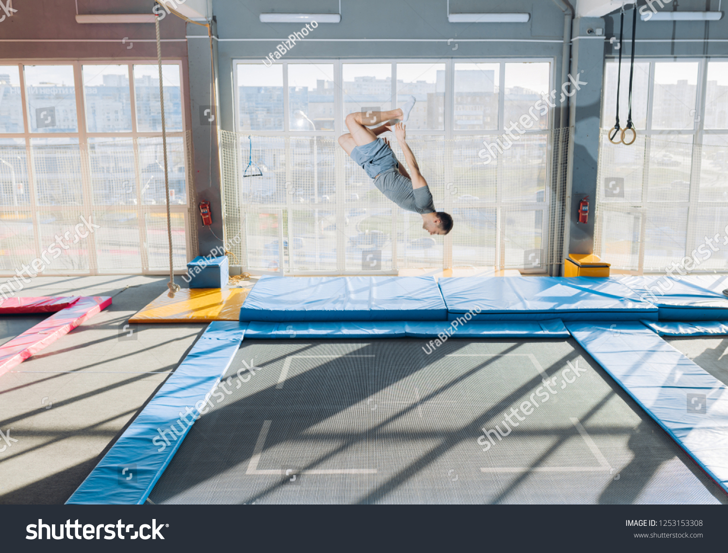 young fit flexible guy doing complex somersault on the trampoline. full length side view shot. copy space. stunt at sky park #1253153308