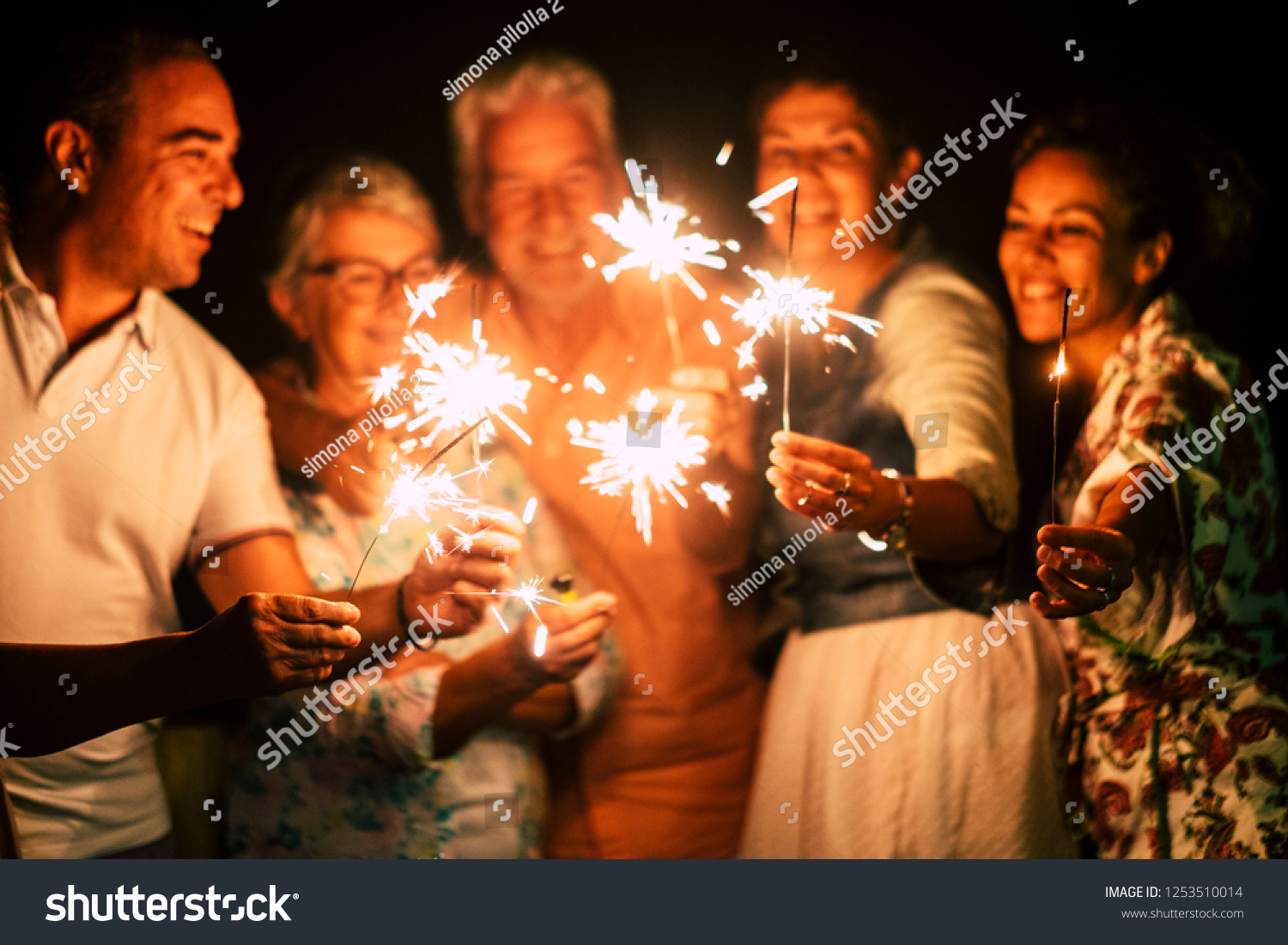 group of people have fun celebrating together new year eve or birthday with sparkles light and fireworks in friendship outdoor at evening time - family and friends different ages celebrate friendly  #1253510014