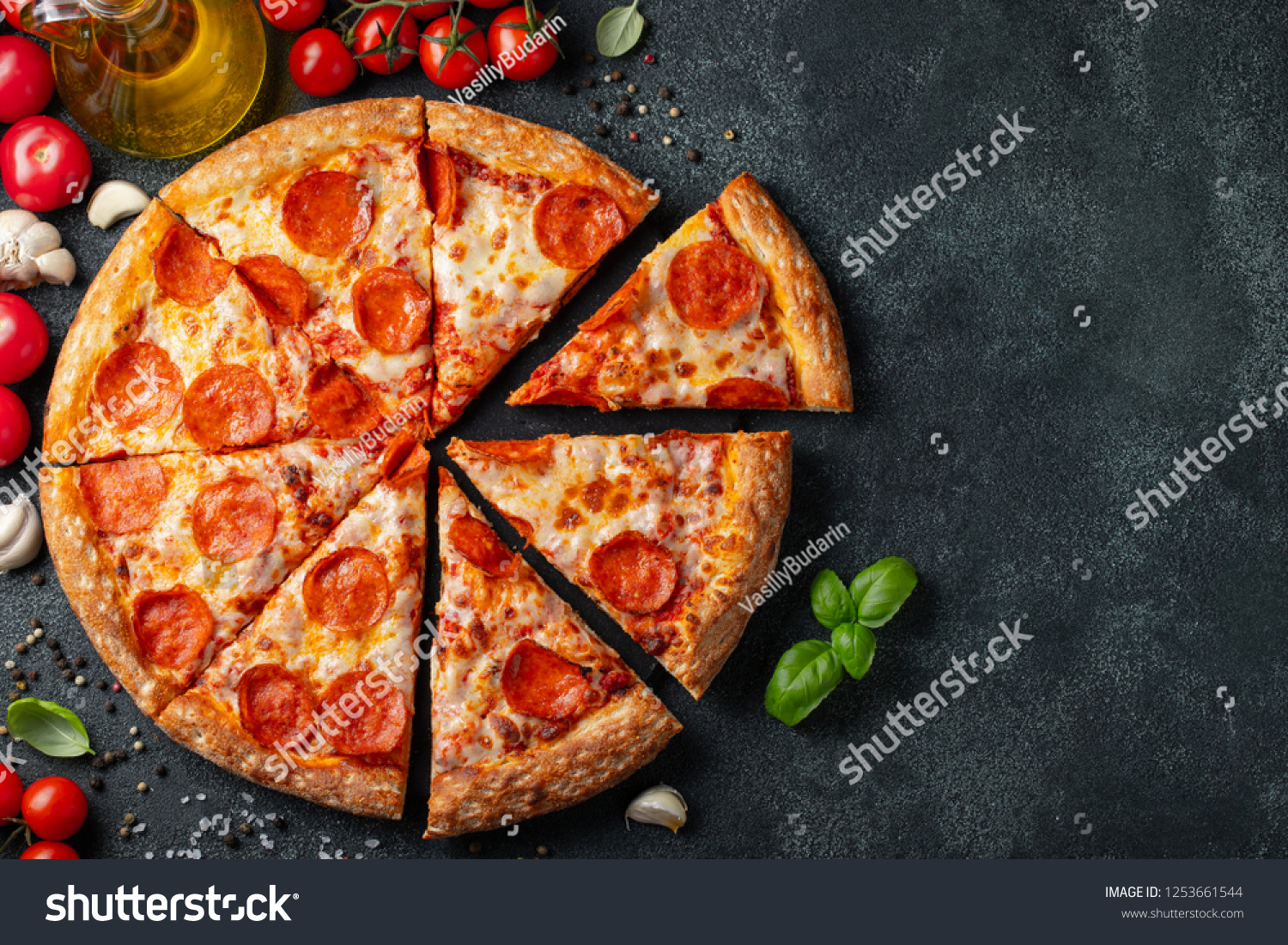 Tasty pepperoni pizza and cooking ingredients tomatoes basil on black concrete background. Top view of hot pepperoni pizza. With copy space for text. Flat lay #1253661544