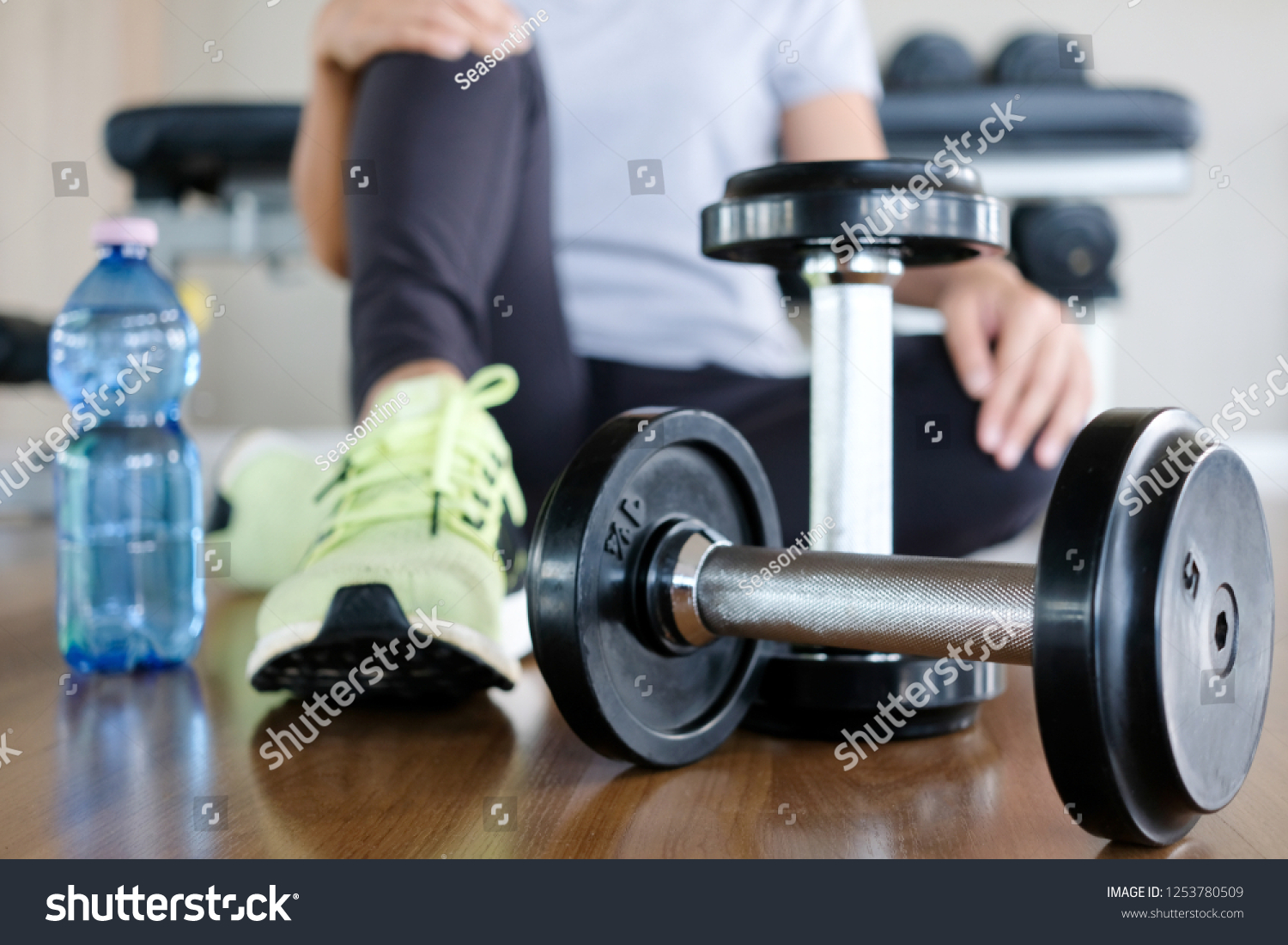 Woman exercise by personal trainer at gym and then be tired. She sit on floor for rest that dumbbell in front of her. Women wearing sport shoes. #1253780509